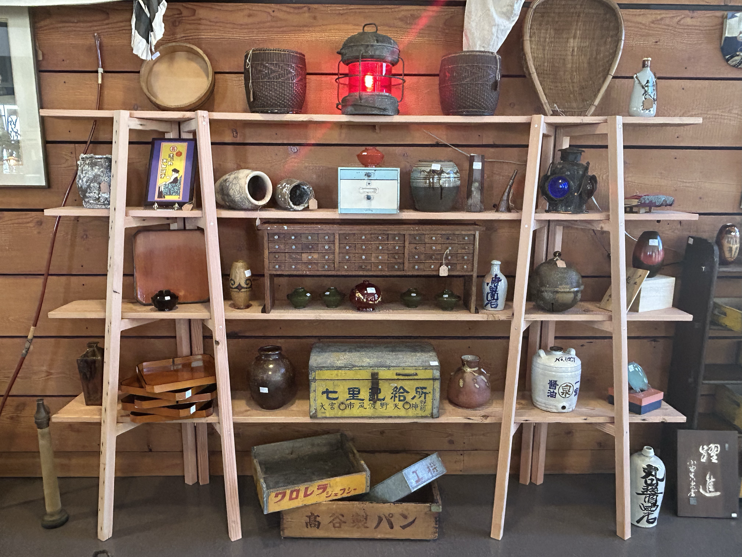 Wall-mounted shelving featuring Japanese antique small objects, including ship lamp, containers, tools, and boxes, arranged as a quiet still-life composition.