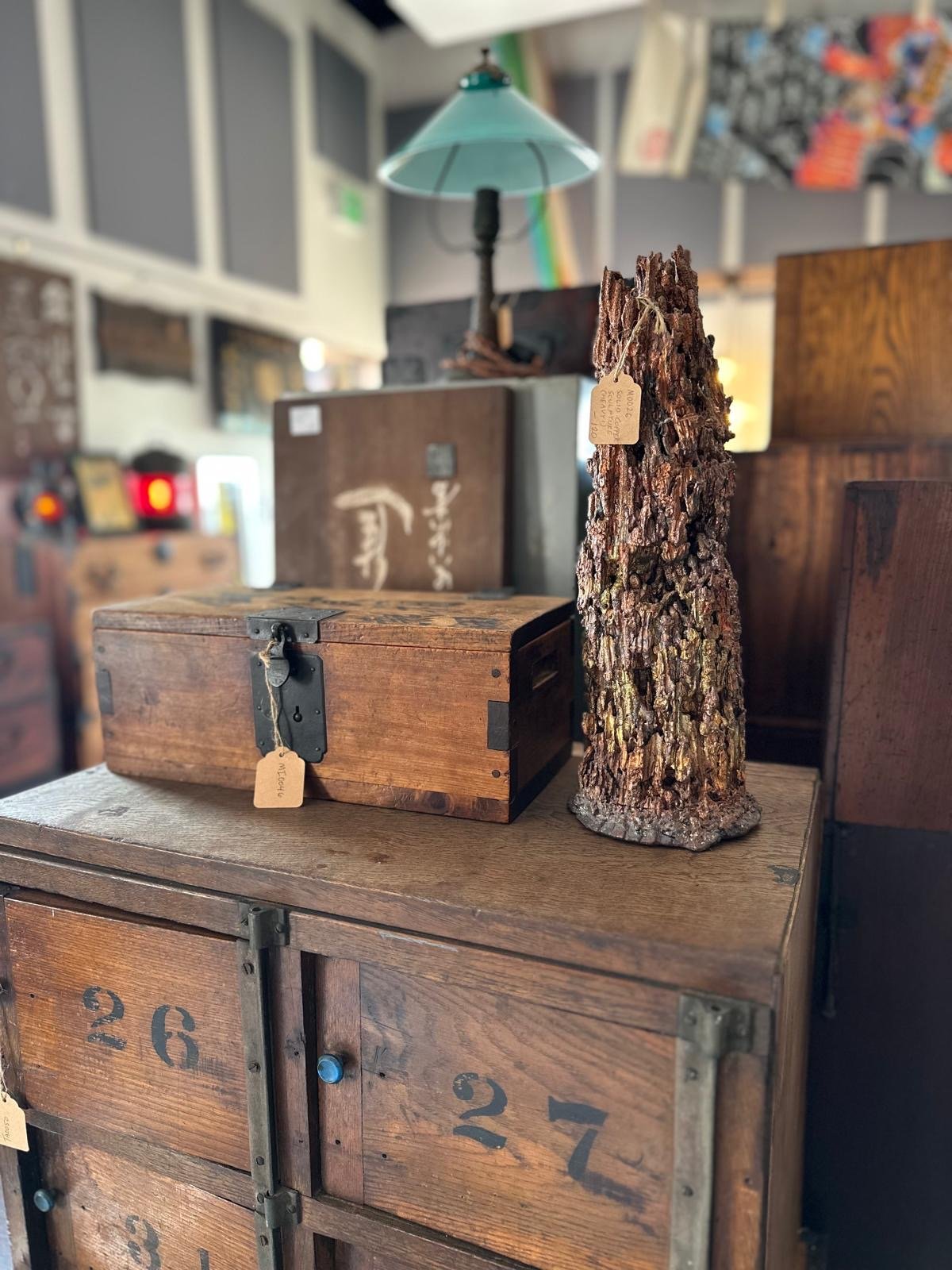 Detail view of a Japanese wooden storage box displayed alongside a solid copper sculptural form, highlighting surface texture, grain, and material contrast. Wooden shoe locker