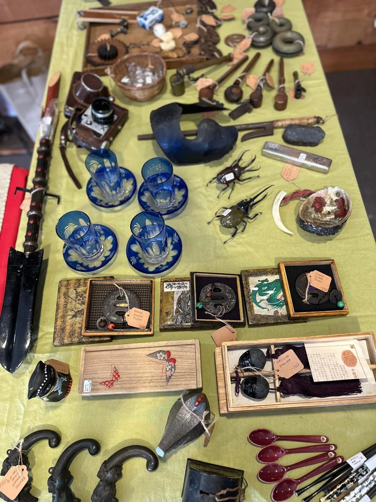 Top-down view of a curated selection of Japanese antique small objects including tools, glassware, metalwork, and decorative items arranged together to show material variety and everyday use.
