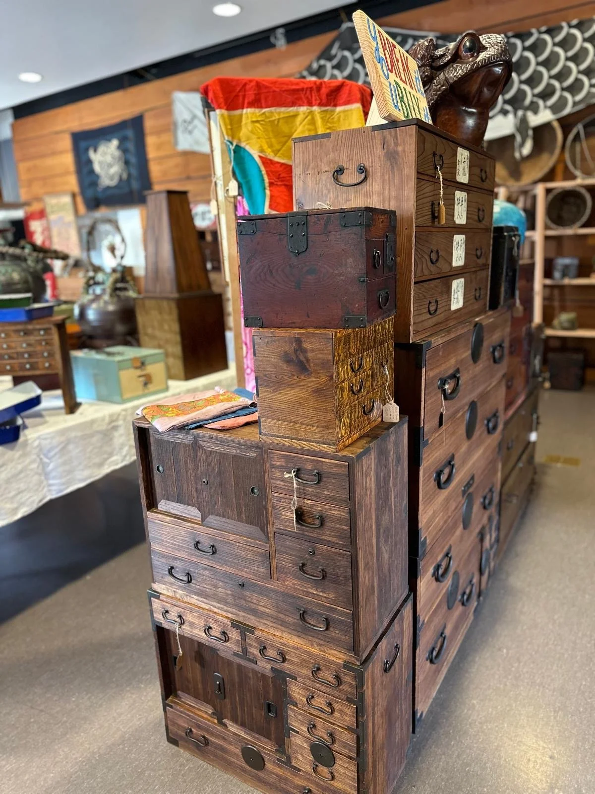Vertical arrangement of Japanese tansu chests and wooden storage boxes, showing traditional joinery, iron hardware, and surfaces worn through decades of use.