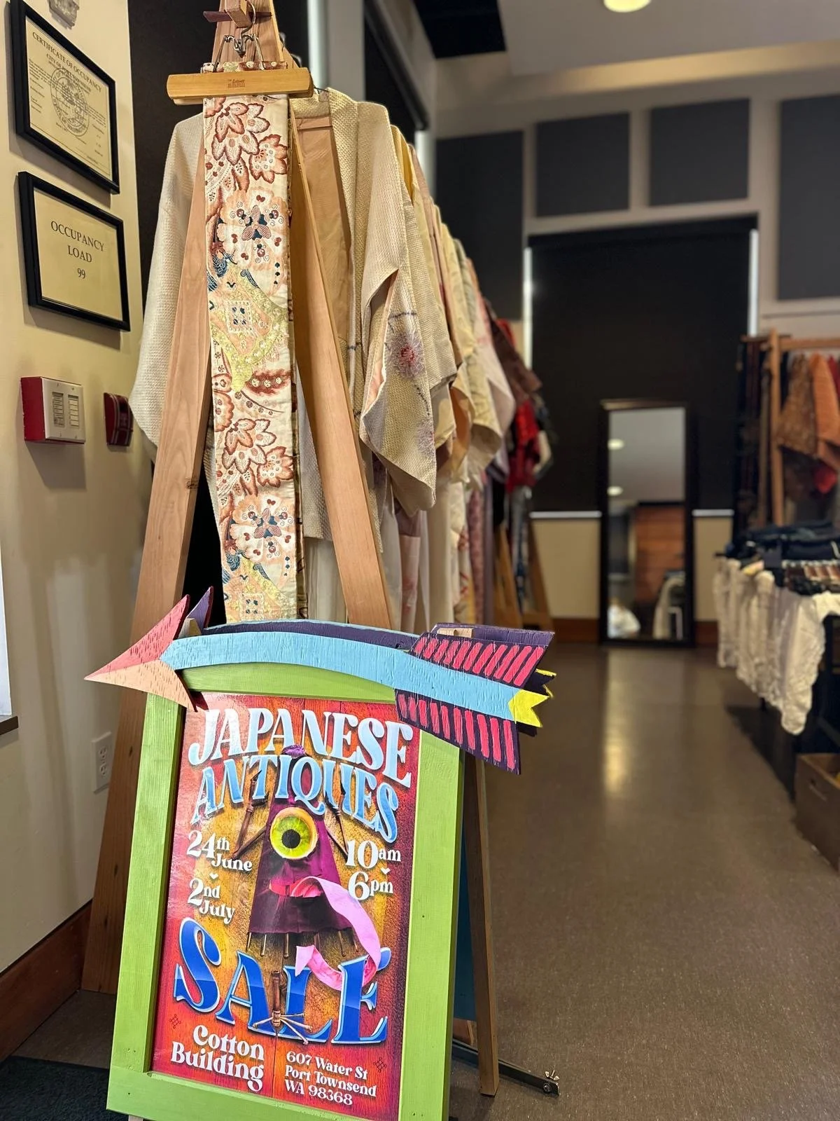 Display of Japanese antique textiles and garments hung on a wooden rack, emphasizing fabric texture, handwork, and subtle color variation.