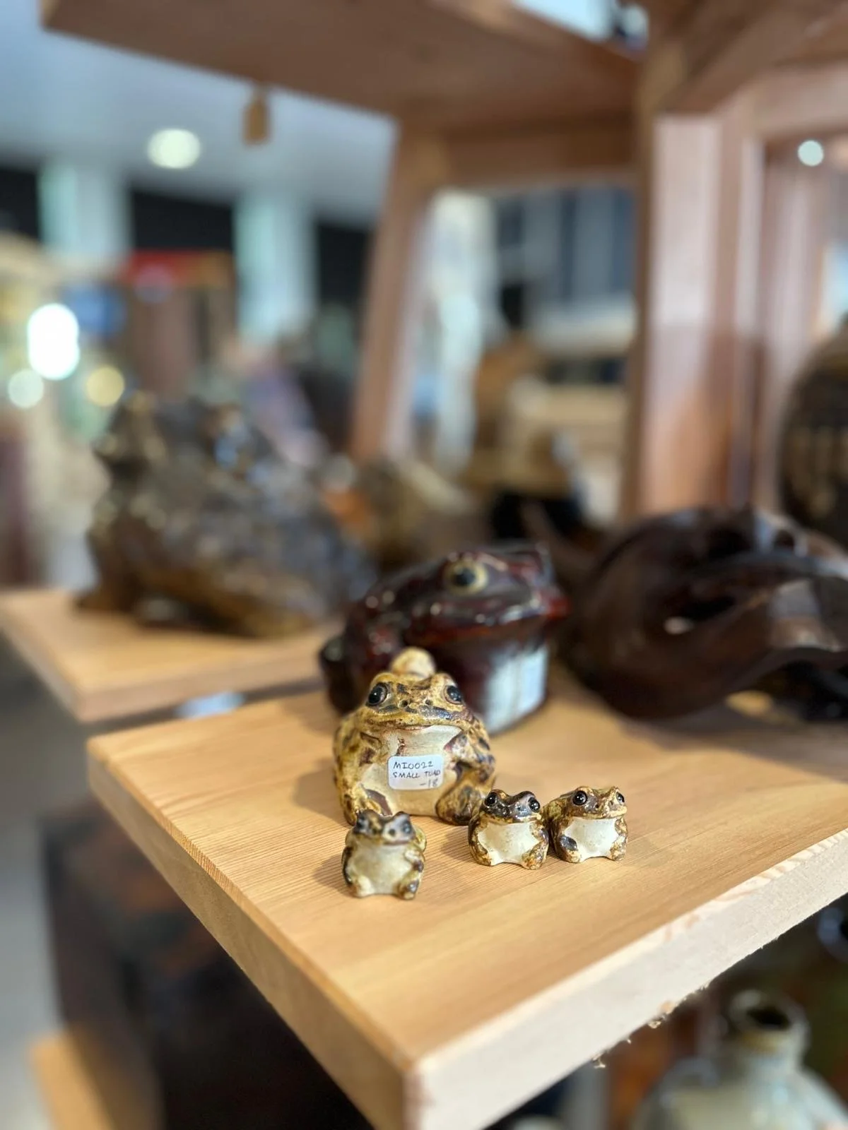 Detail view of Japanese ceramic frog figures displayed on a wooden shelf, showing hand-formed features, glazed surfaces, and playful folk character.