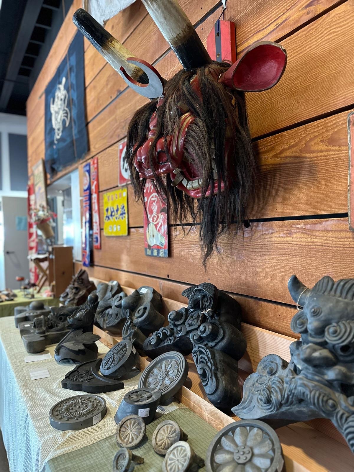Traditional Japanese lion dance mask displayed alongside antique roof tile fragments and architectural ornaments, showing age, hand-carved detail, and surface patina.