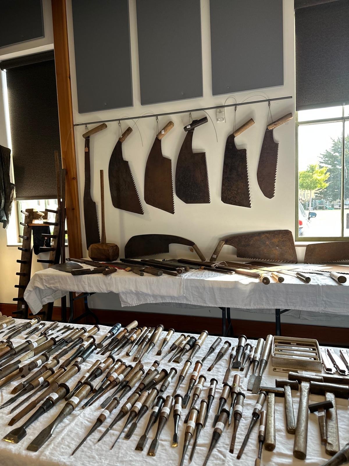 Display of antique Japanese saws, chisels, and hand tools hung and arranged for a pop-up exhibition, highlighting traditional woodworking forms and materials.
