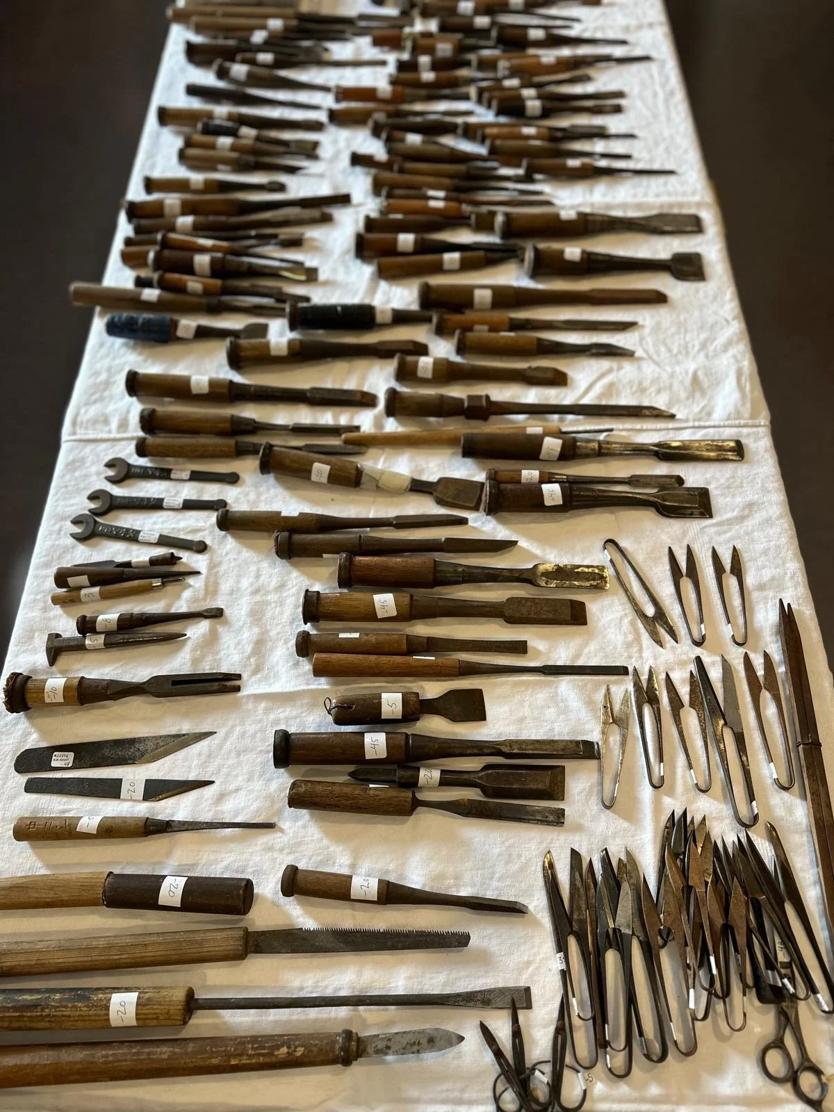 Top-down view of antique Japanese chisels and small woodworking tools arranged by type and size, showing forged steel blades and wooden handles with age patina.