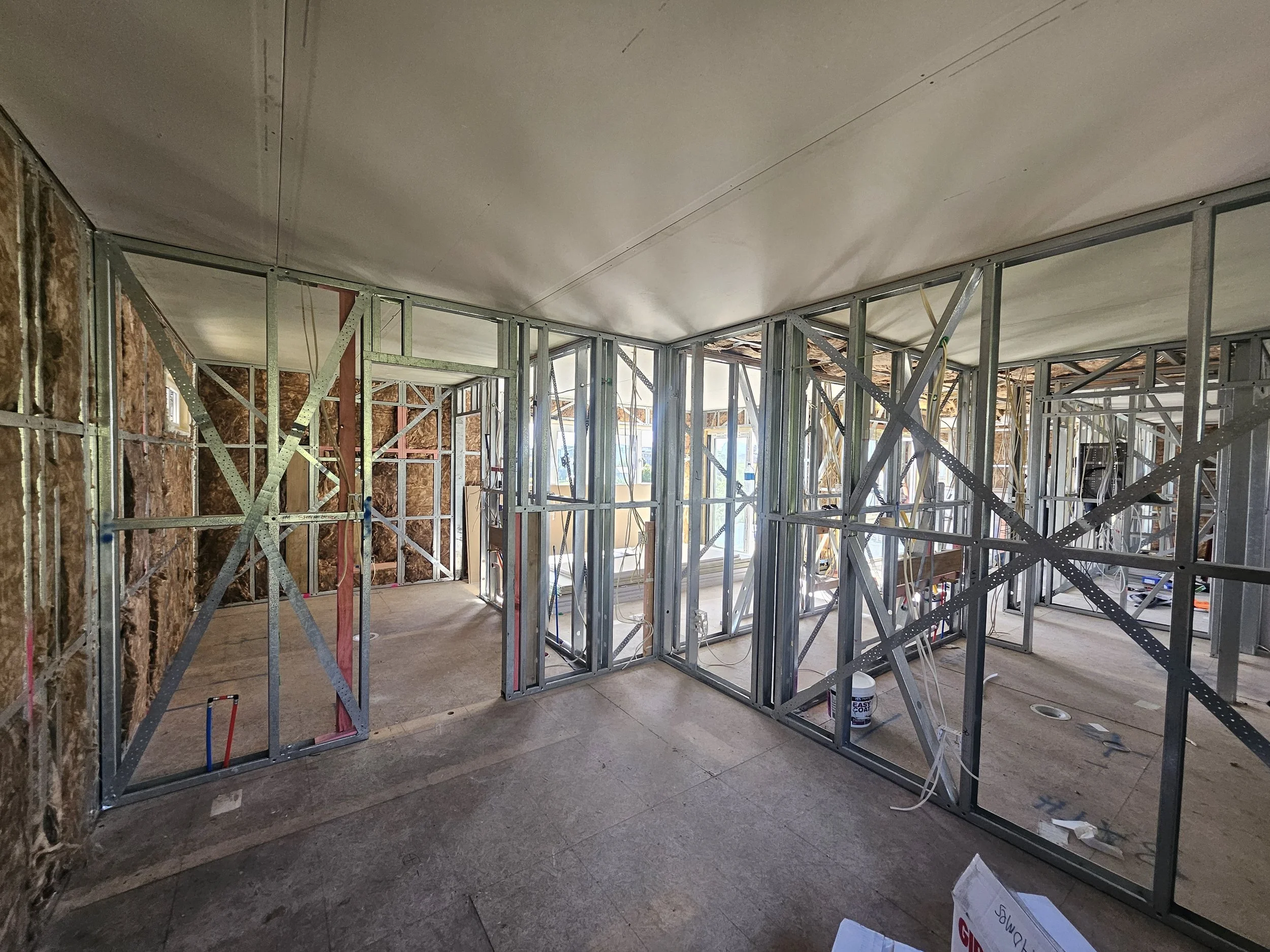 Interior view of a building under construction with exposed metal framing, insulation on walls, and no finished walls or ceiling.