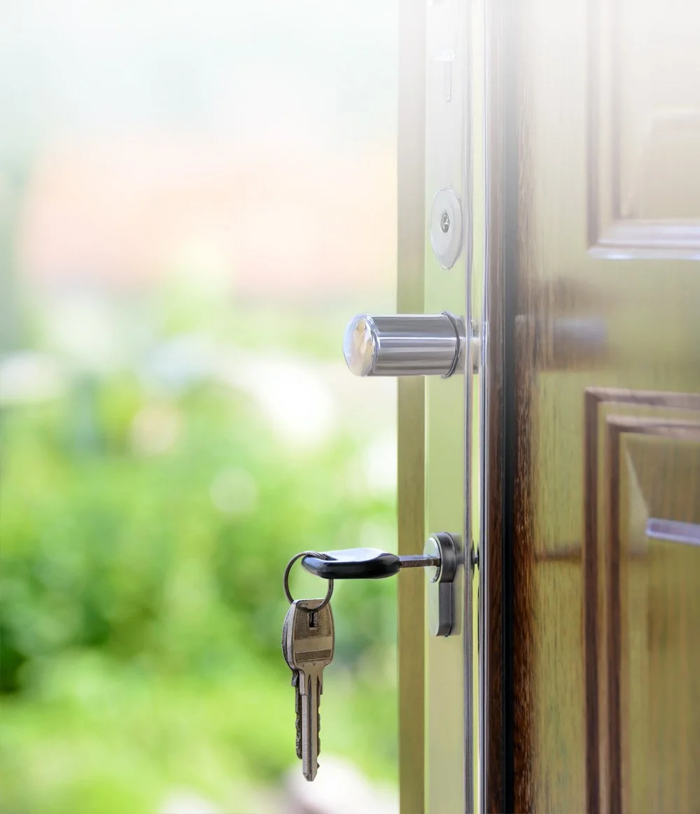 A set of keys hanging from a door lock with a blurred background of green outdoor scenery.