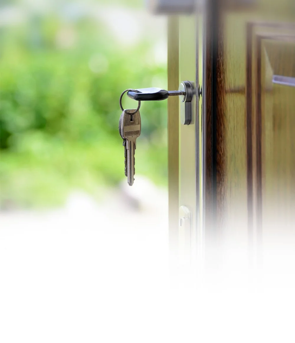 A set of keys hanging from a door lock with a blurred background of green outdoor scenery.