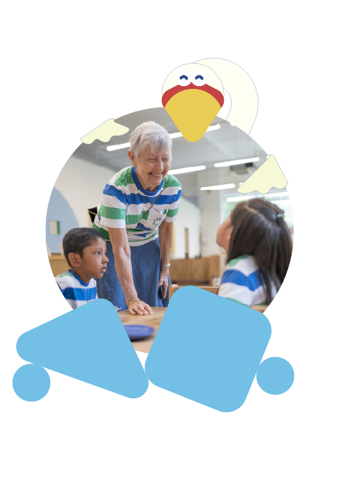 An elderly woman with white hair smiling and engaging with two children at a table in a classroom or daycare setting, with cartoon chicken illustrations overlayed on the image.