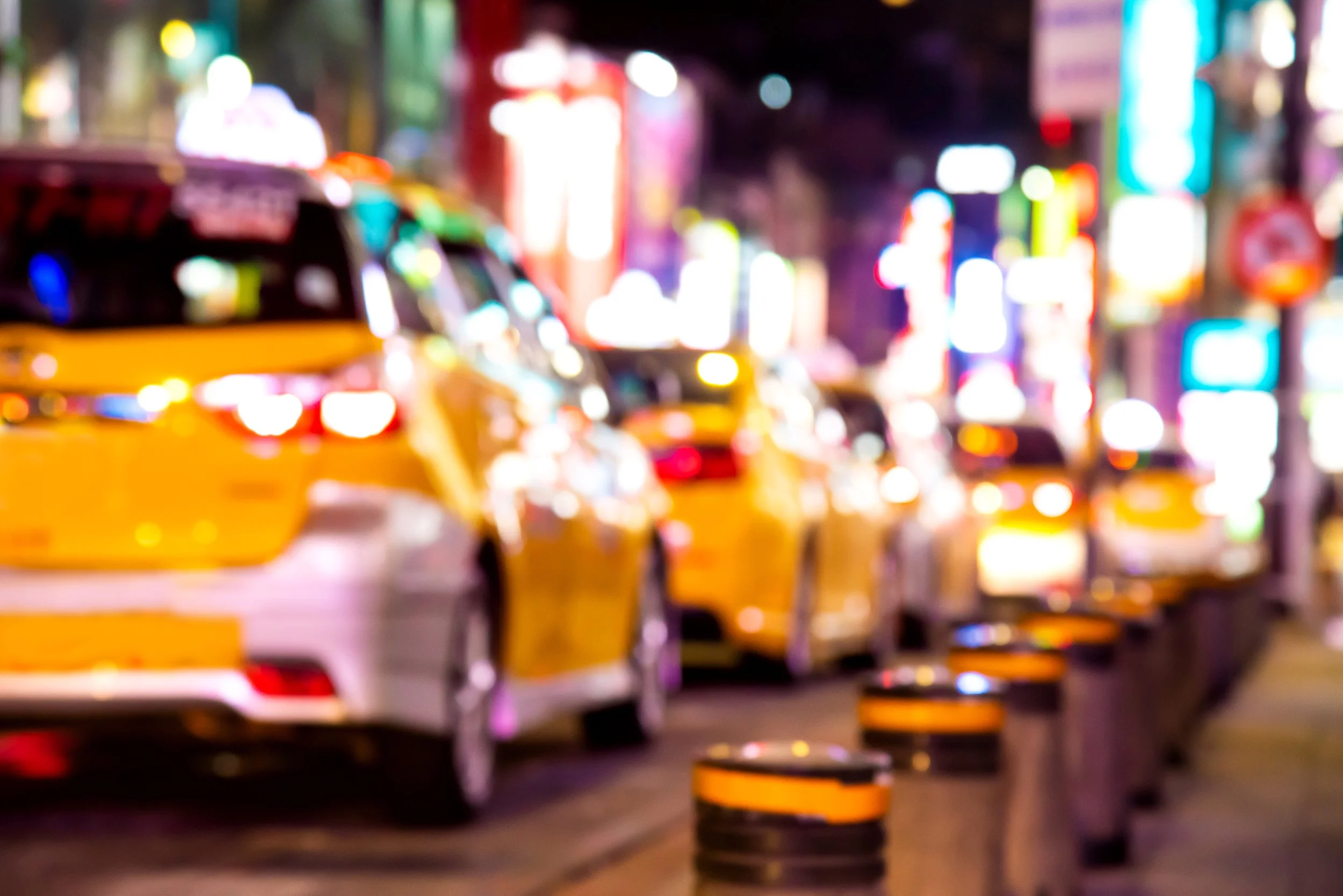 Blurred view of yellow taxis in a busy city street at night with bright, colorful lights and illuminated signs.