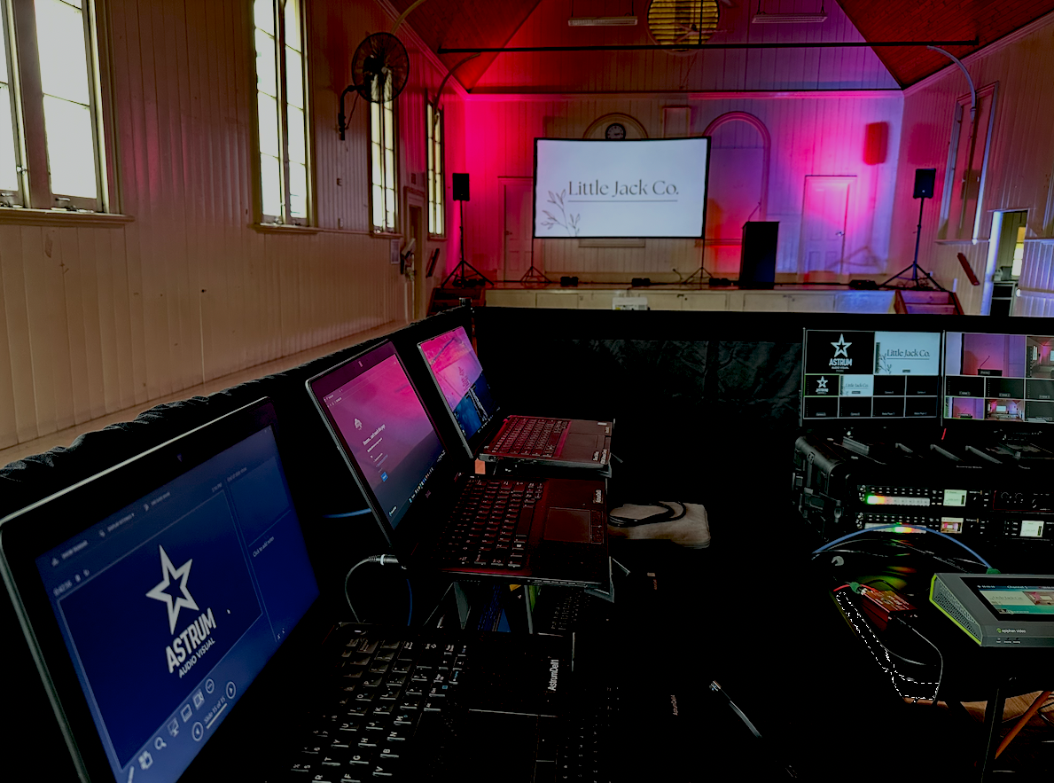 Event stage setup with a large screen displaying content. Community event with cameras and lectern with microphone and speakers