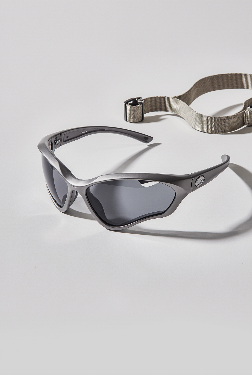 Sport sunglasses with dark lenses and a strap, placed on a white surface.