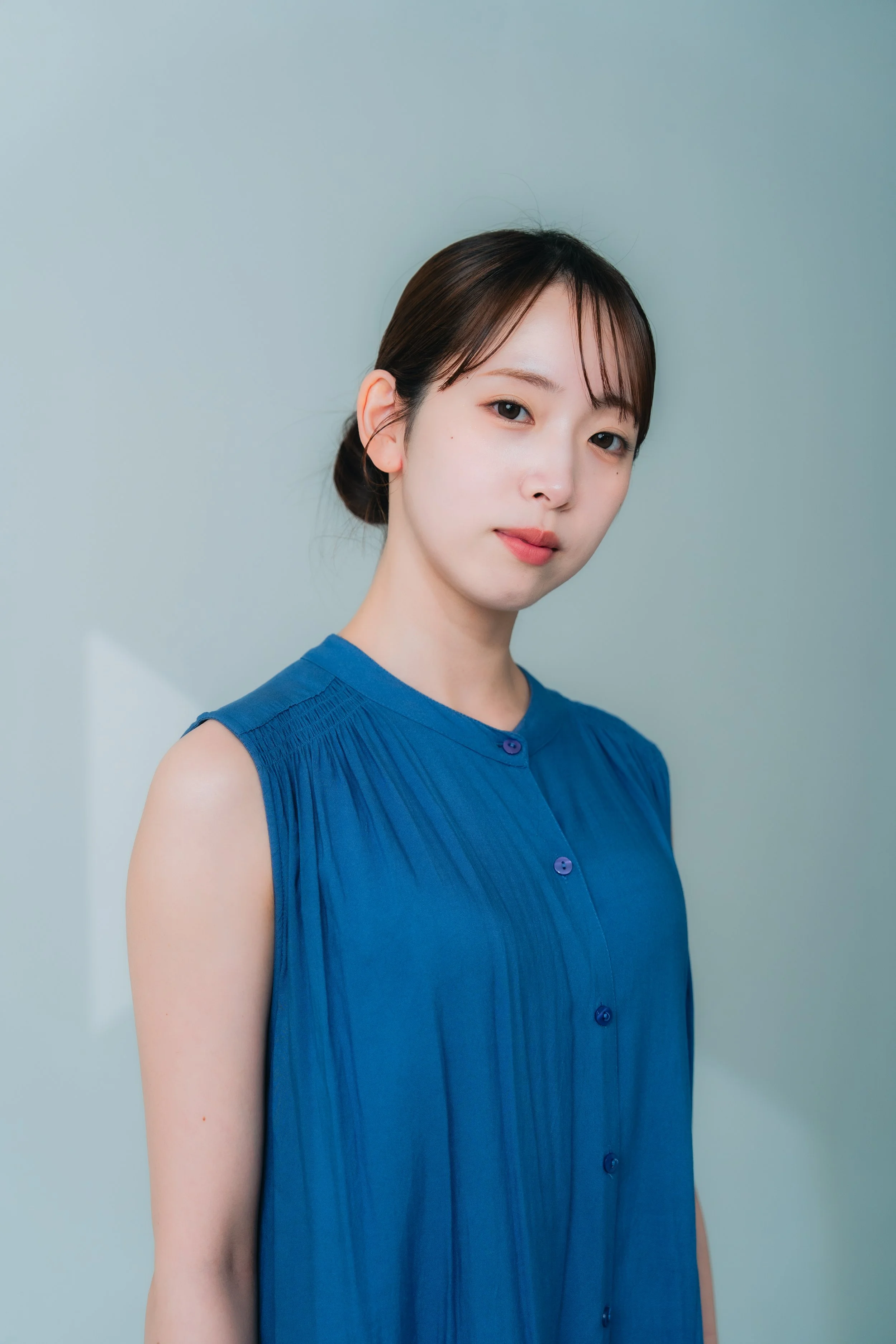 青色のドレスを着た若い女性の正面の写真。背景は薄い緑色。
