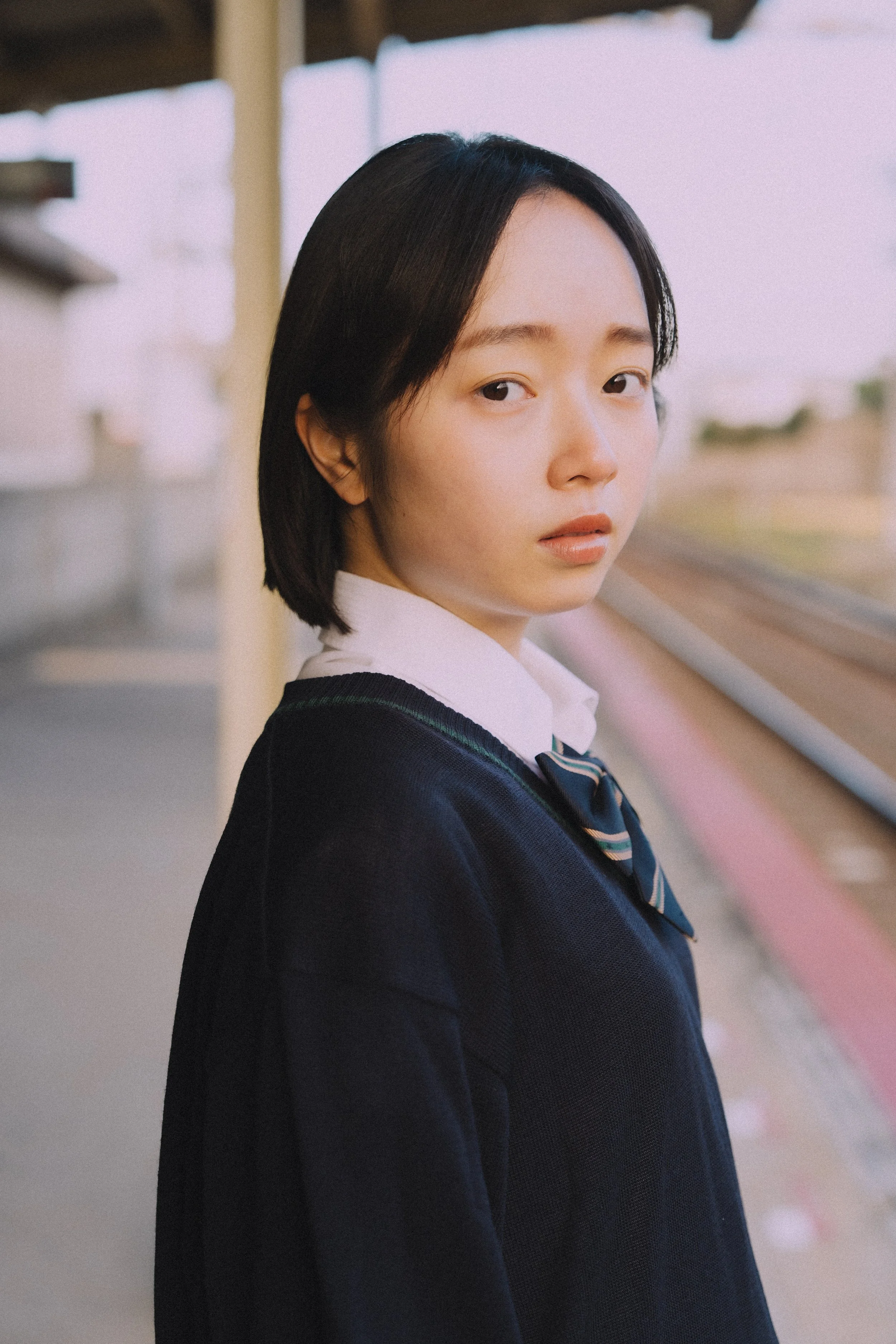 電車のホームで制服を着た若い女性が側に立っている風景
