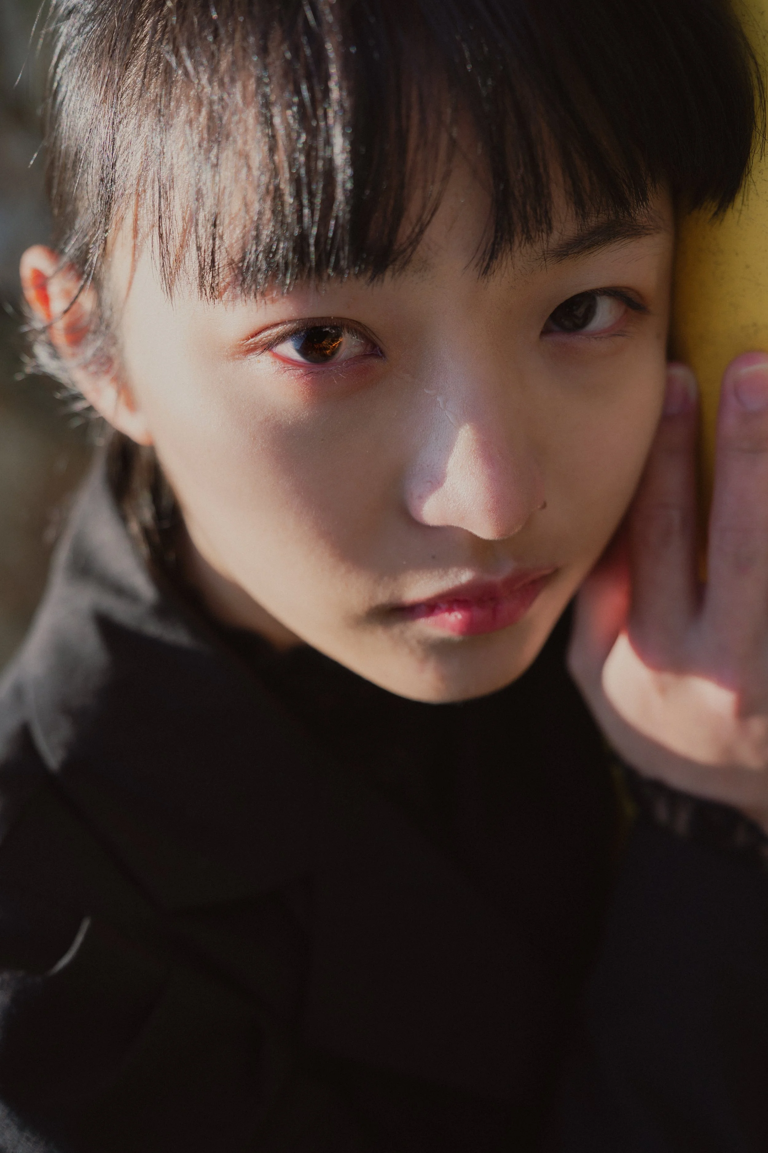 少年の顔のクローズアップ写真。左目が見え、右目の上に髪がかかっている。少年は黒い服を着ている。