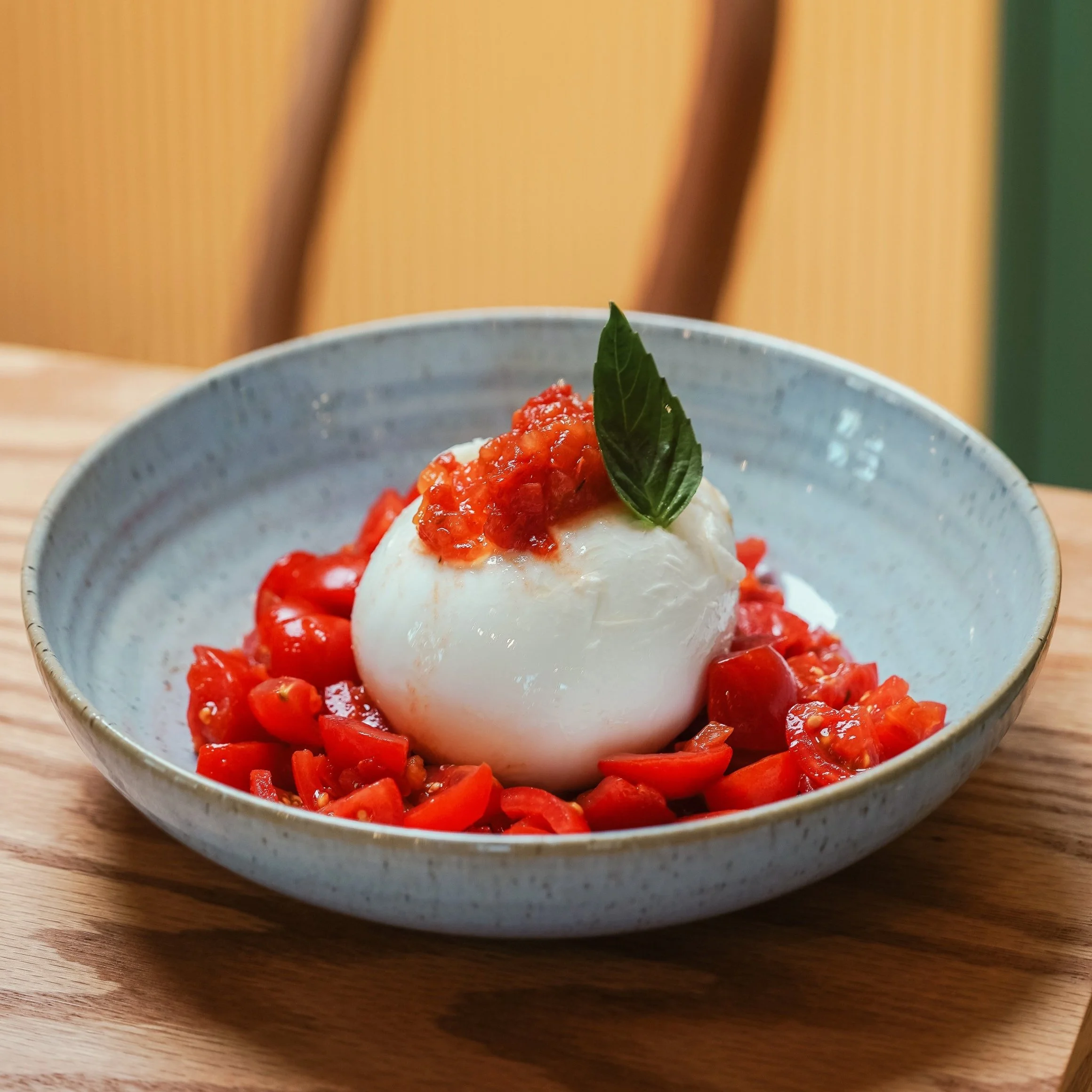 Bowl with a poached egg topped with tomato sauce, surrounded by chopped tomatoes and garnished with a basil leaf.