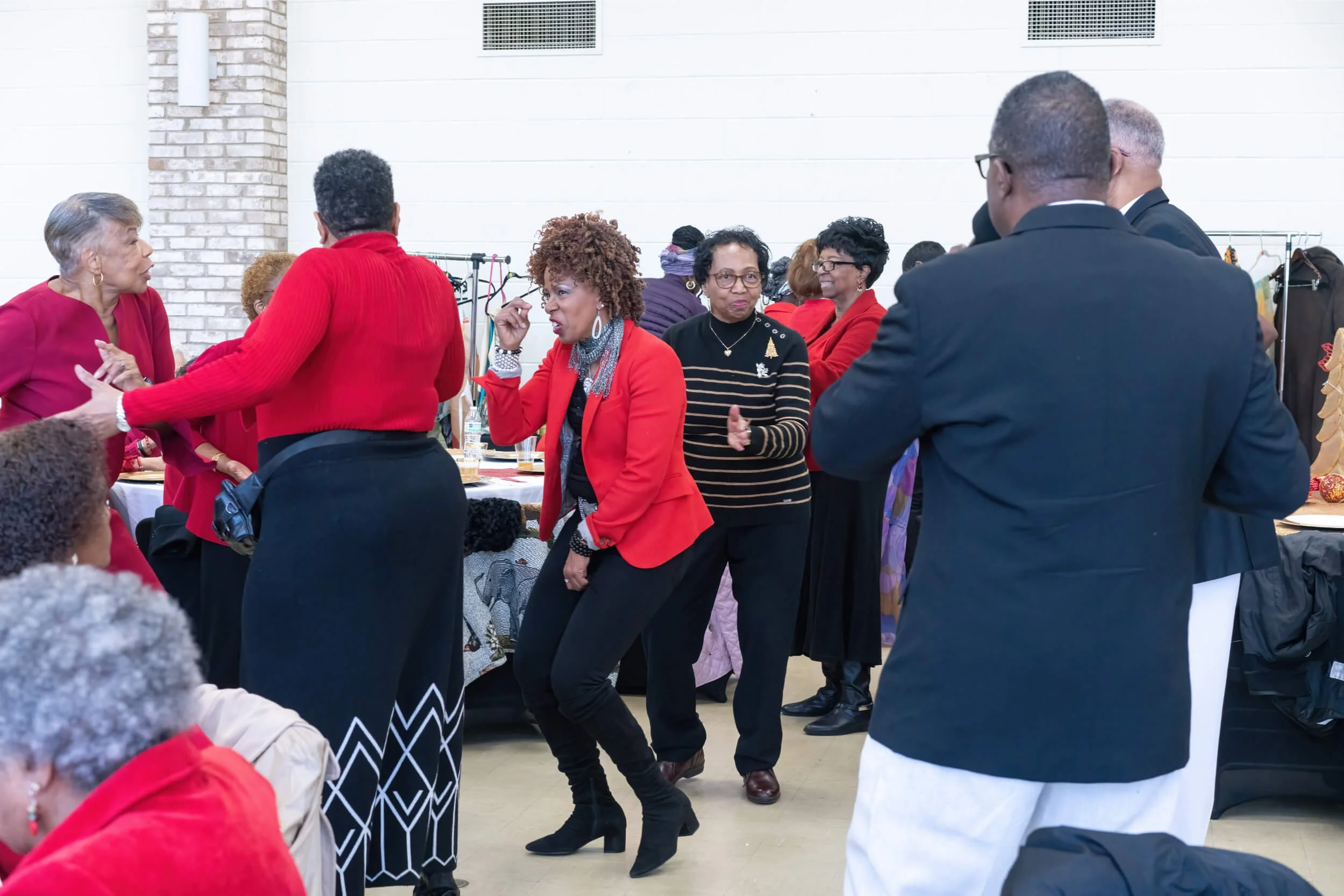 Group of people dancing and socializing at a party, with some women wearing red and black outfits and men in suits.