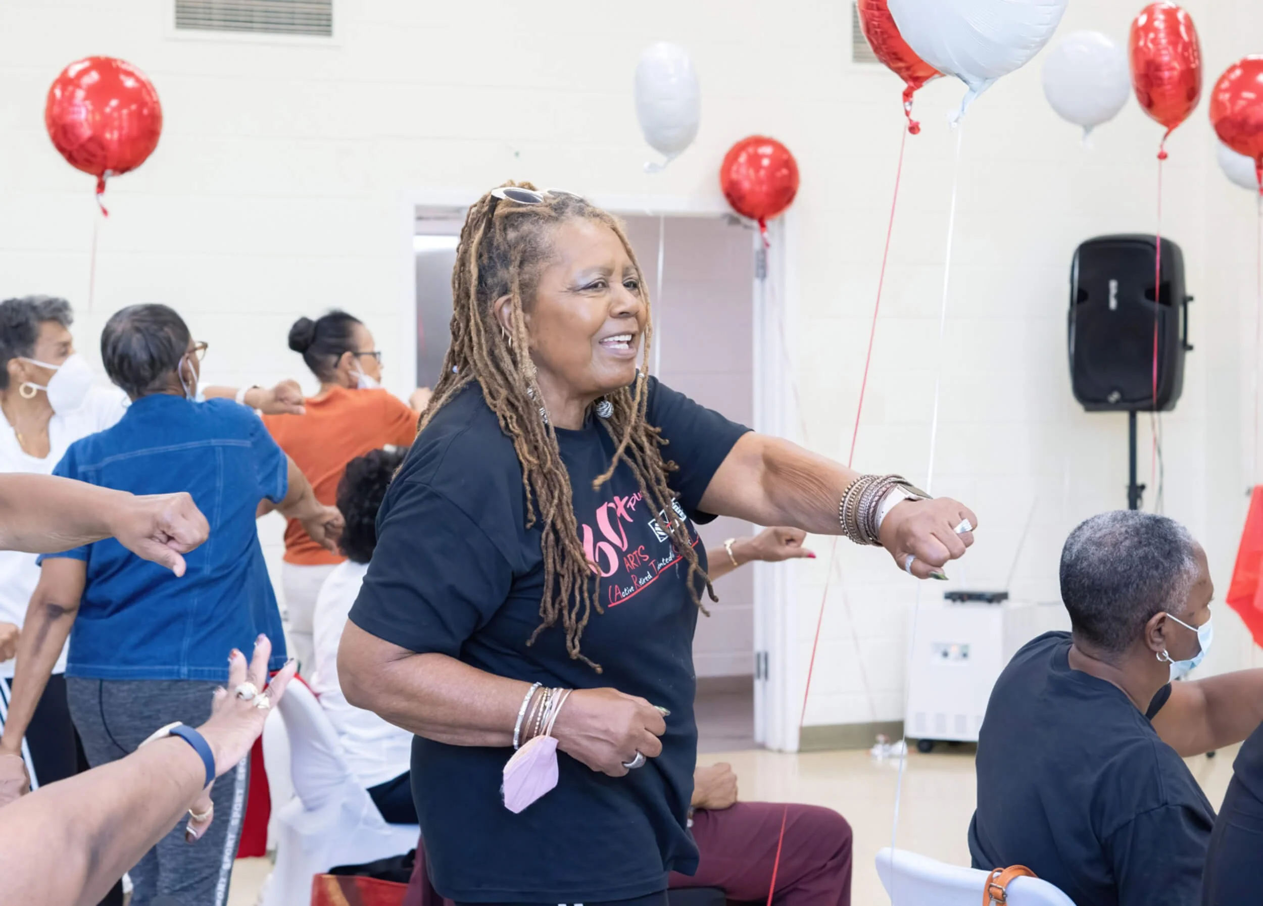 A group of people participating in a dance or exercise activity indoors, with red and white balloons tied to the ceiling.