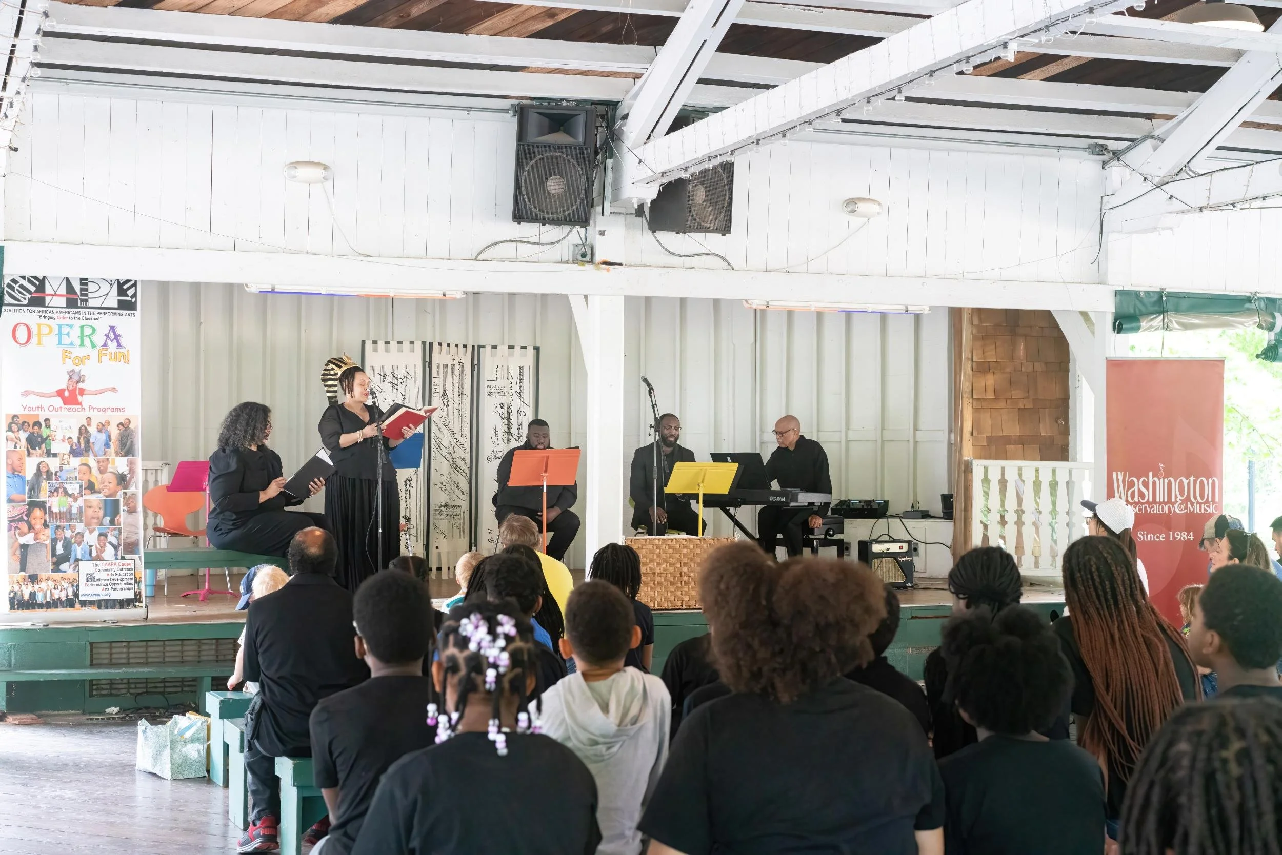 A musical performance on stage at Washington Observatry and Music, with a group of four musicians and a singer, in front of an audience in an indoor venue.