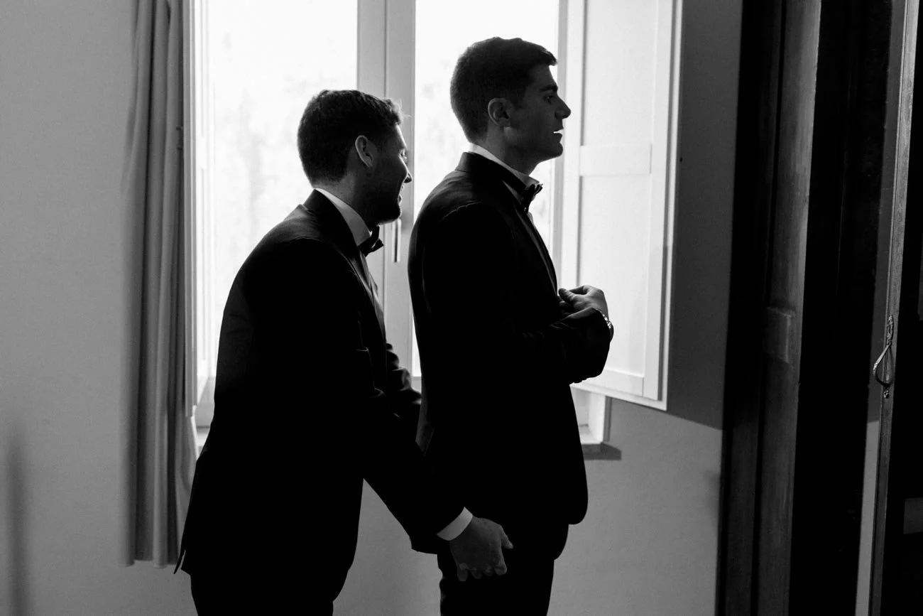 Due uomini in abiti eleganti si tengono per mano mentre si preparano a entrare in una stanza.