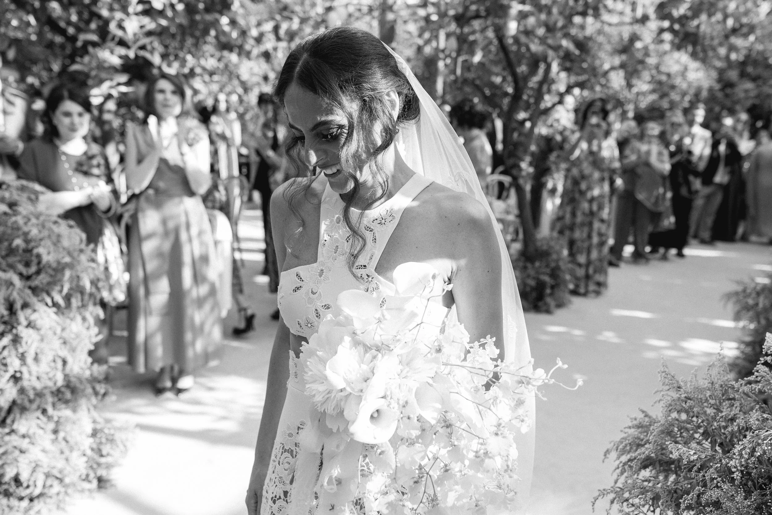 Una sposa sorride durante il suo matrimonio, circondata da invitati in un giardino.