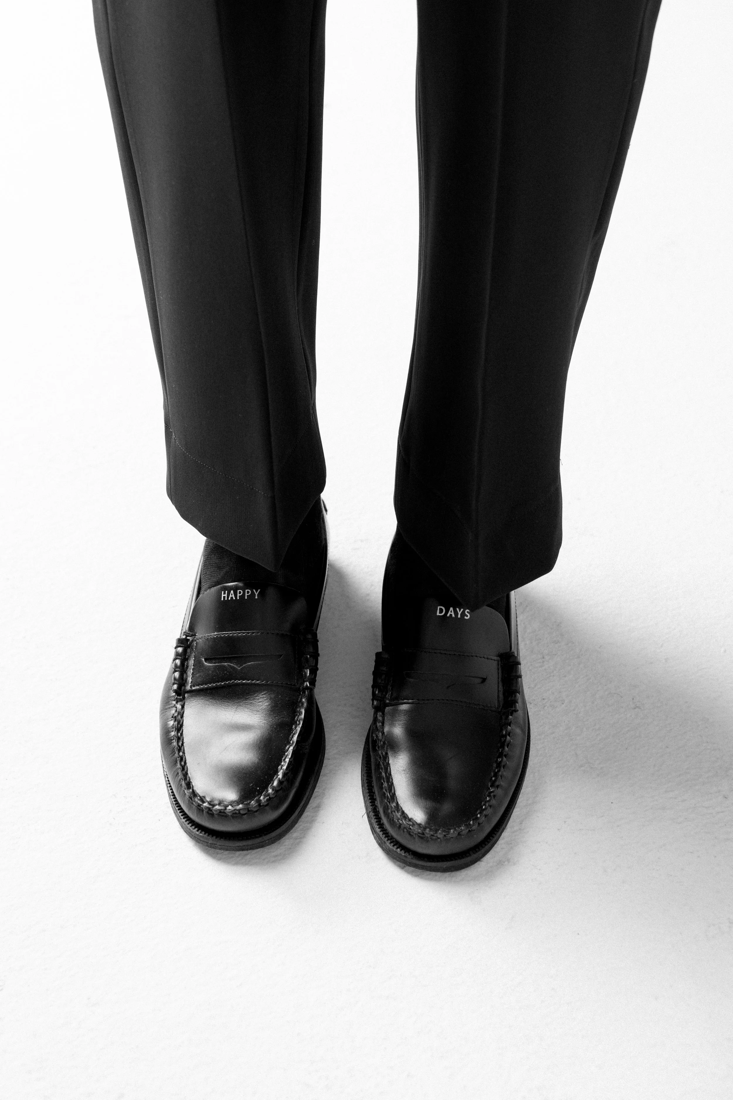 Scarpe nere con scritte 'HAPPY' e 'DAYS' sulla punta, indossate da una persona con pantaloni neri.
