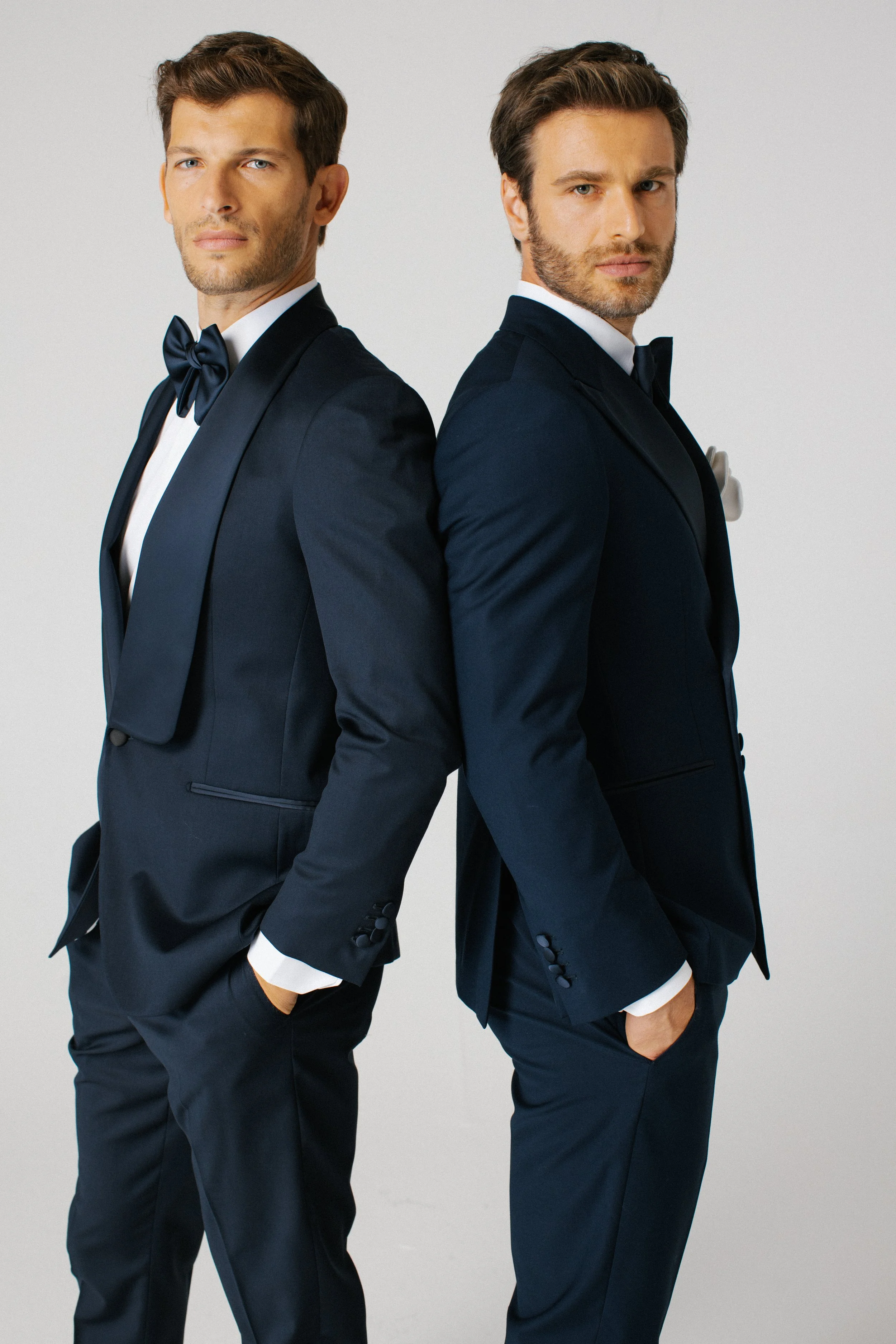 Due uomini in abiti da sera eleganti, uno con papillon e l'altro con cravatta, che si appoggiano con le spalle che si toccano