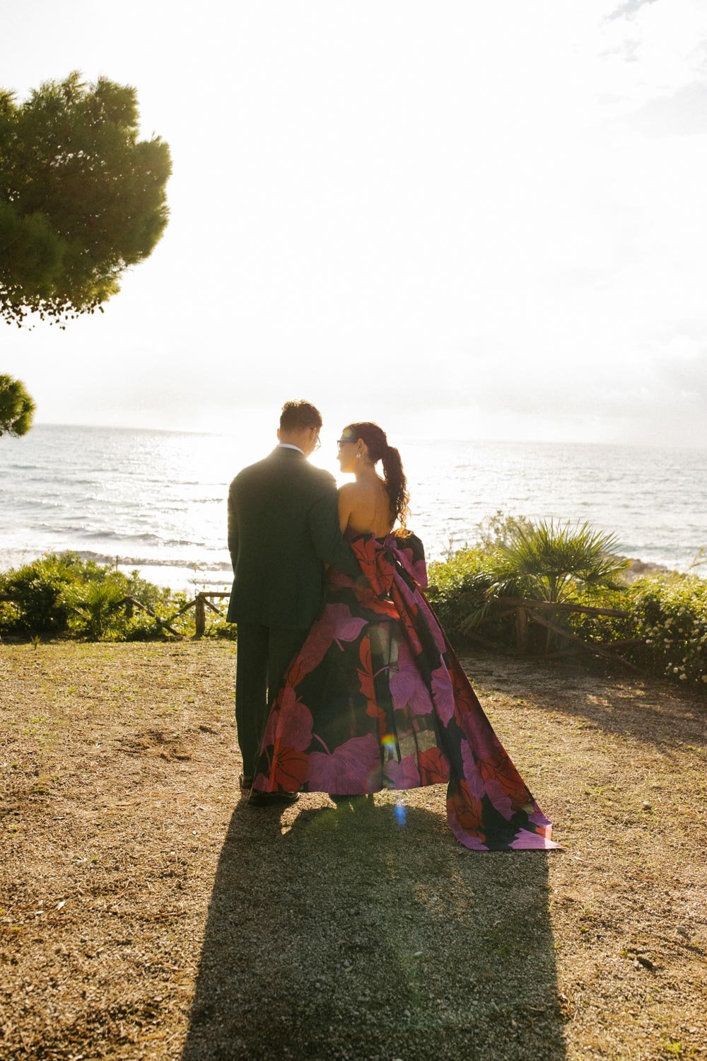 Coppia in abiti eleganti al tramonto sulla spiaggia, vista mare e vegetazione tropicale.