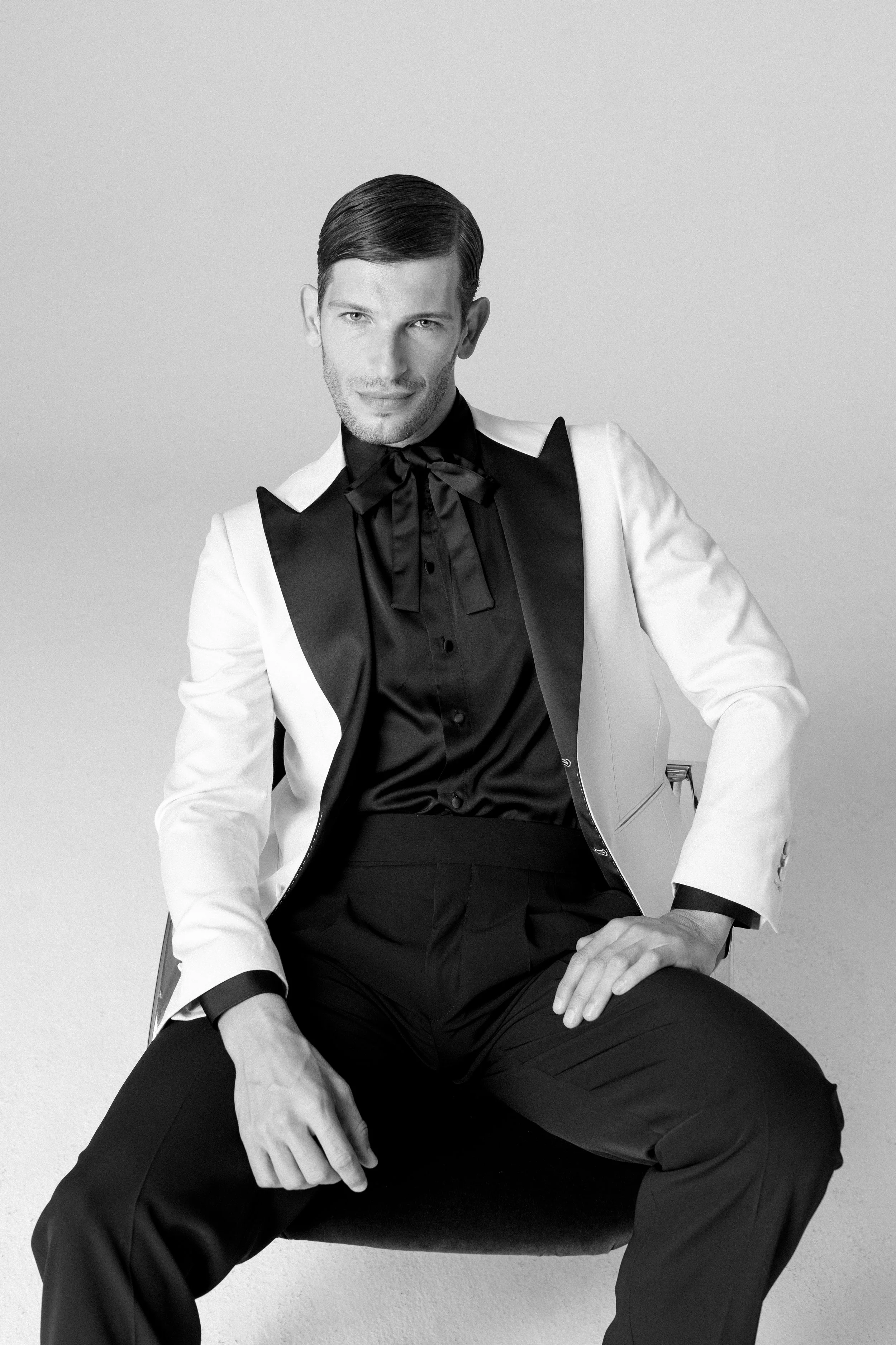 Ragazzo in abbigliamento elegante con giacca bianca e cravatta nera seduto su una sedia