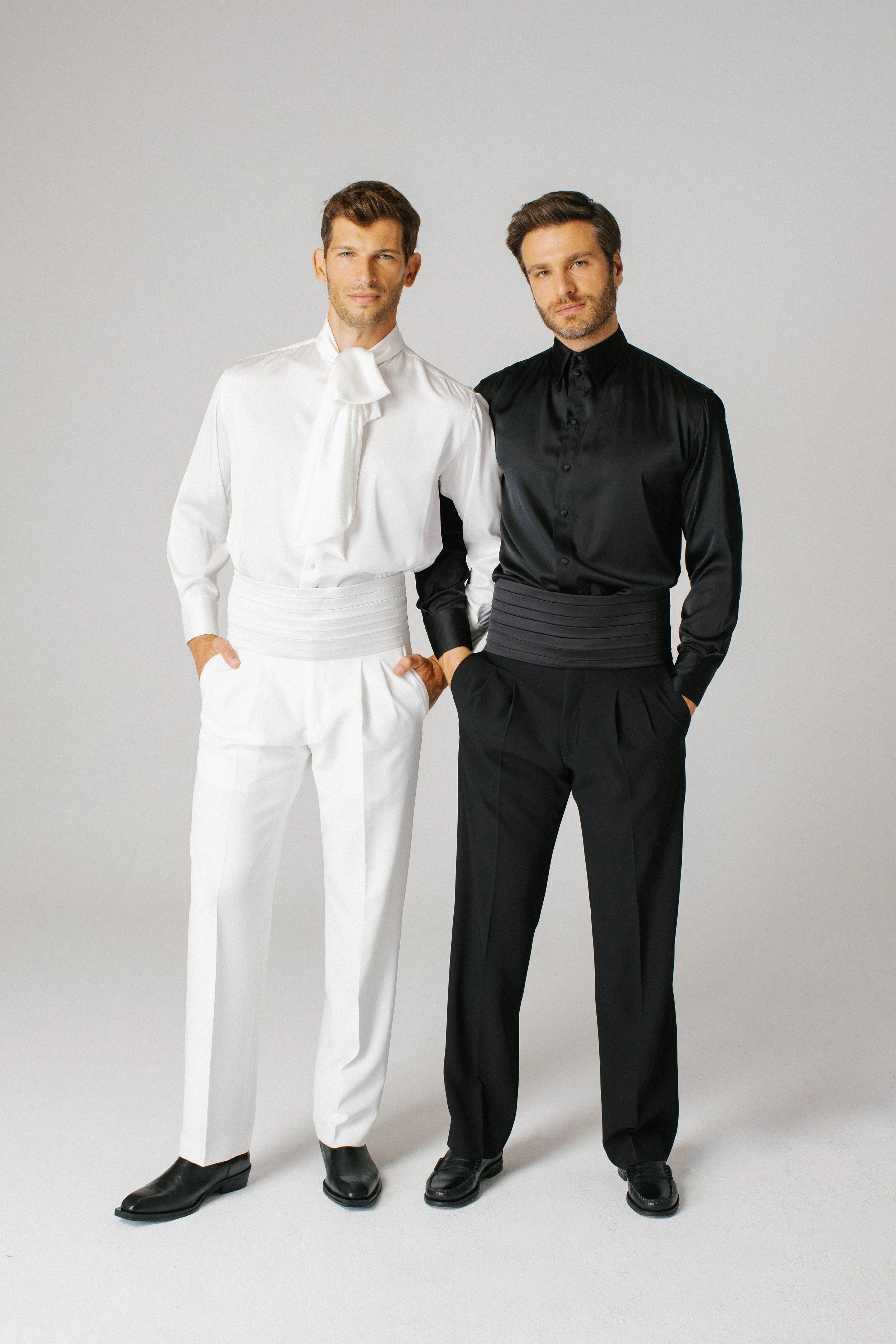 Due uomini eleganti indossano abiti tradizionali Hemingway, uno in completo bianco con cravatta e l'altro in completo nero con camicia in seta.