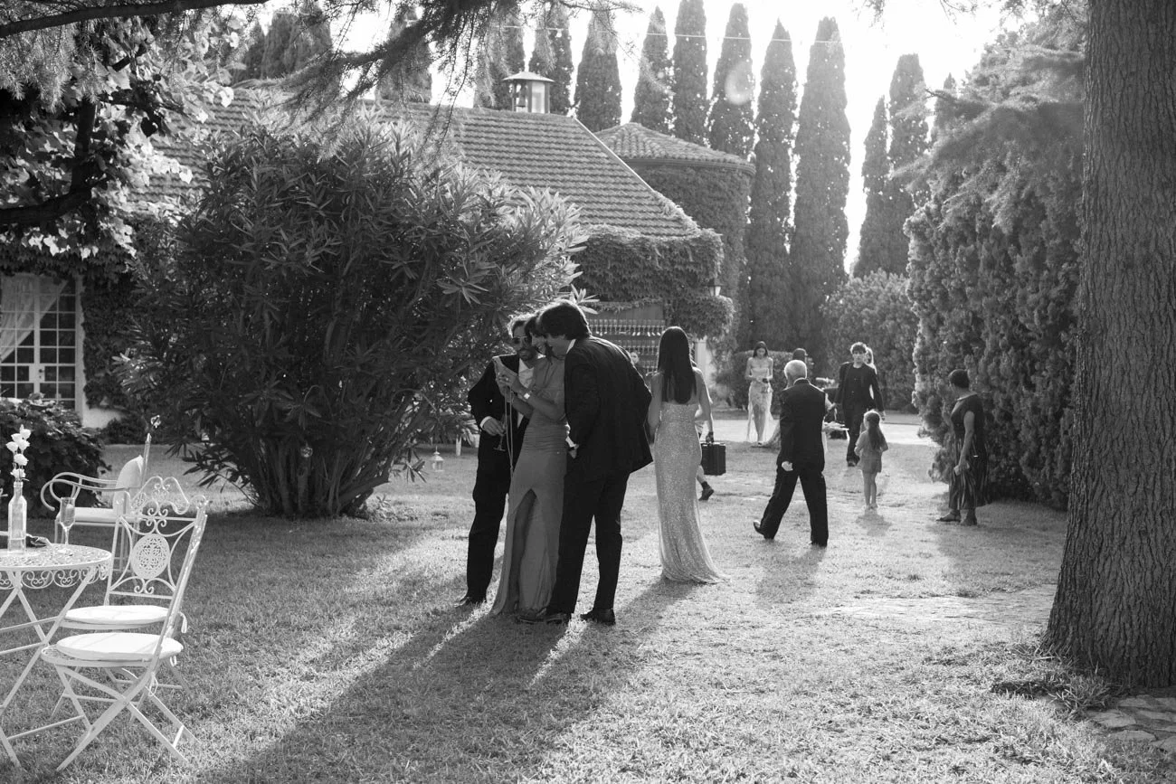Foto in bianco e nero di un giardino con persone vestite elegantemente, probabilmente durante un evento o un matrimonio.