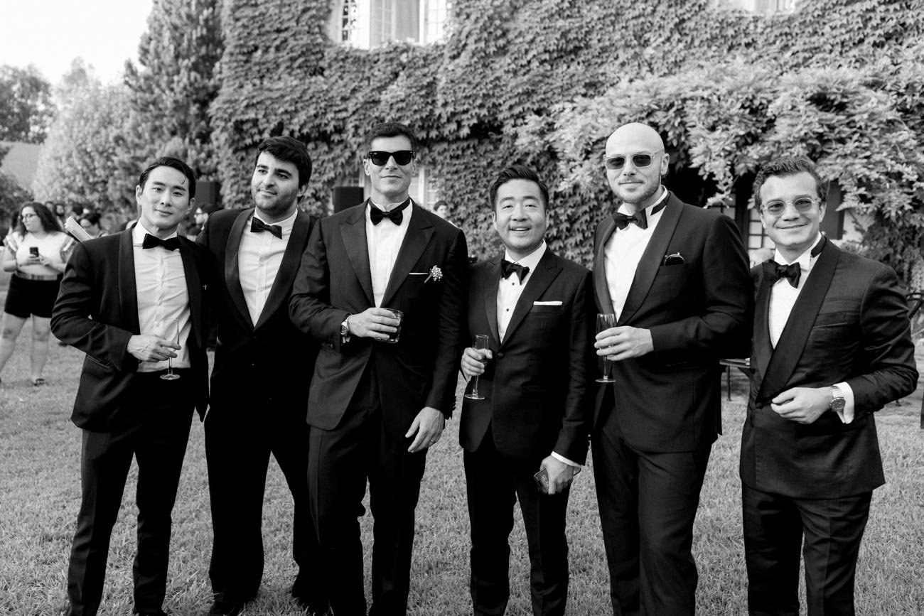 Gruppo di uomini vestiti in smoking durante un evento all'aperto.