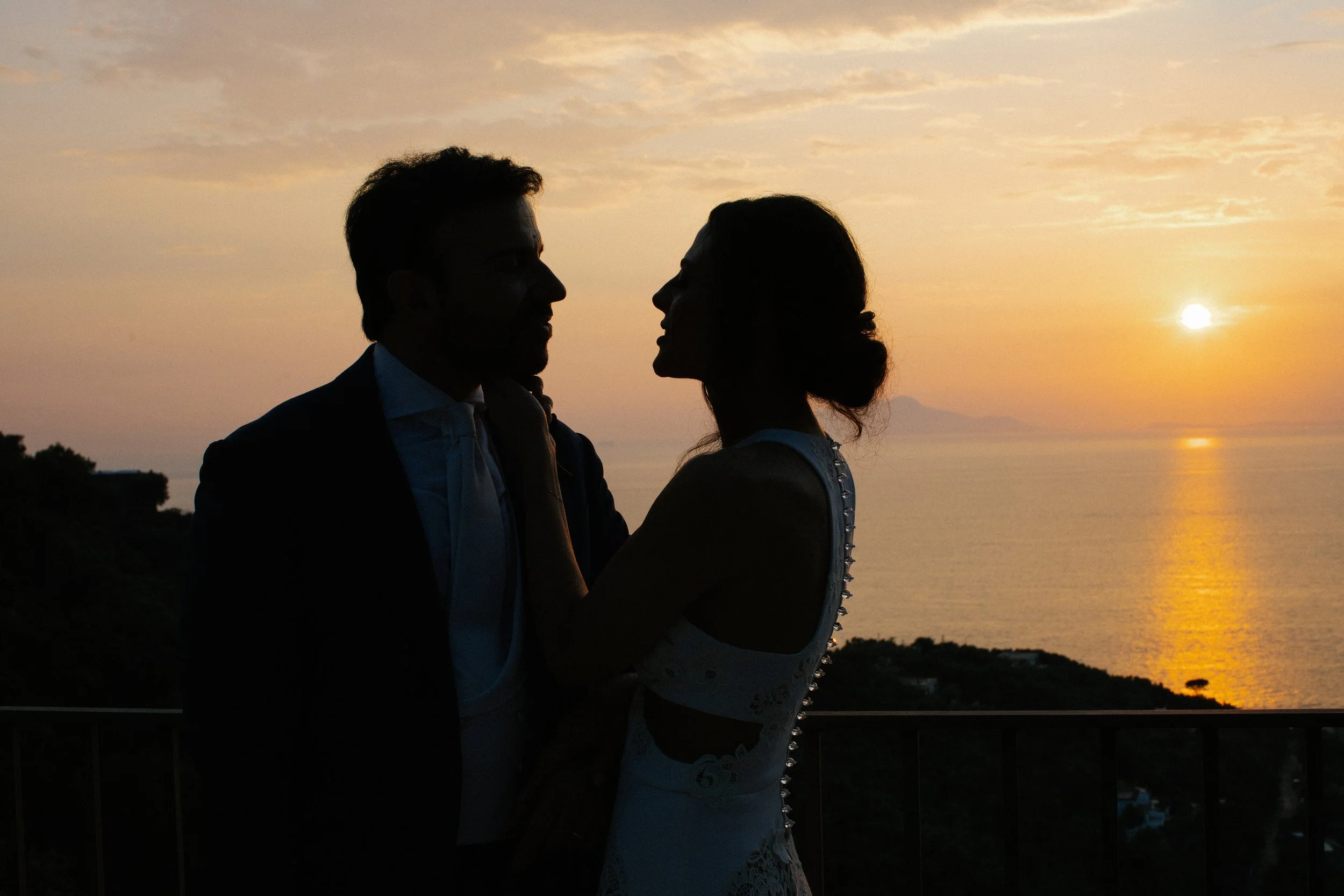 Una coppia si guarda di fronte mentre il sole tramonta sul mare, creando una scena romantica al crepuscolo.