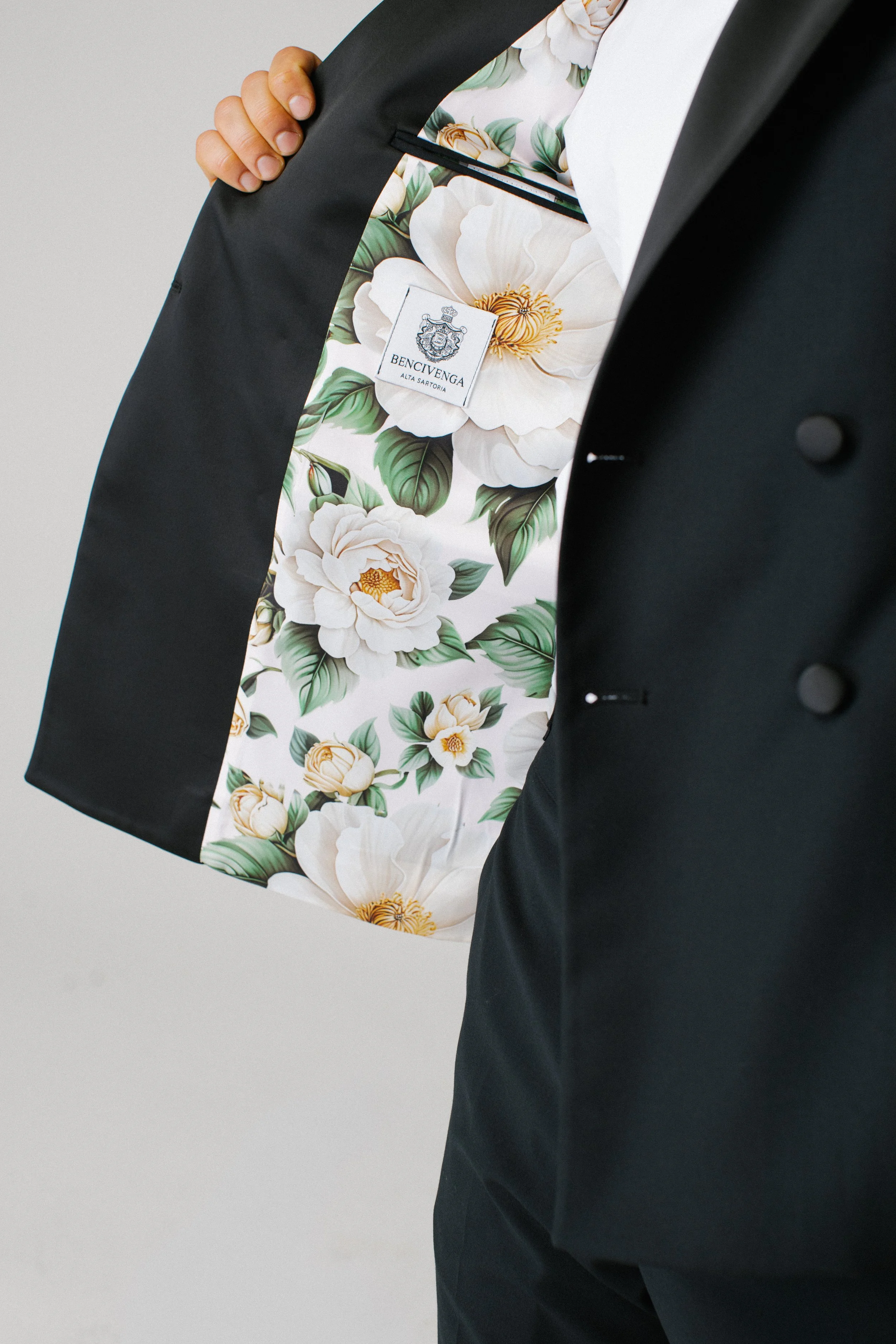 Interno di una giacca elegante con fodera floreale bianca e verde, con etichetta di marca 'Bencivenga Alta Sartoria'.