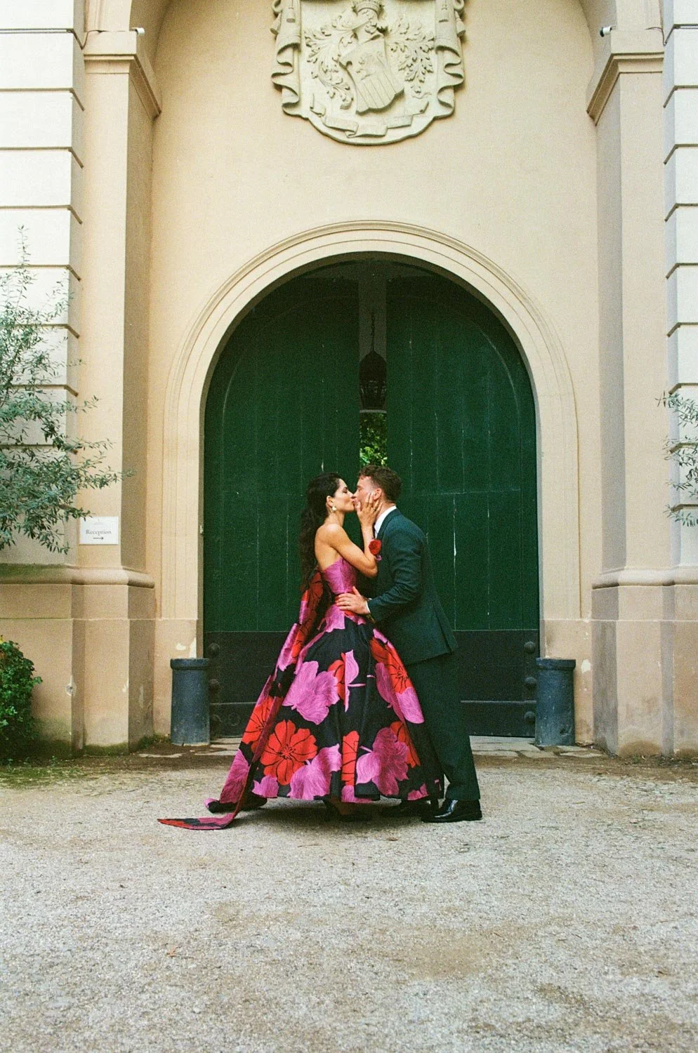 Una coppia di sposi si bacia davanti a una grande porta di colore verde in un cortile.