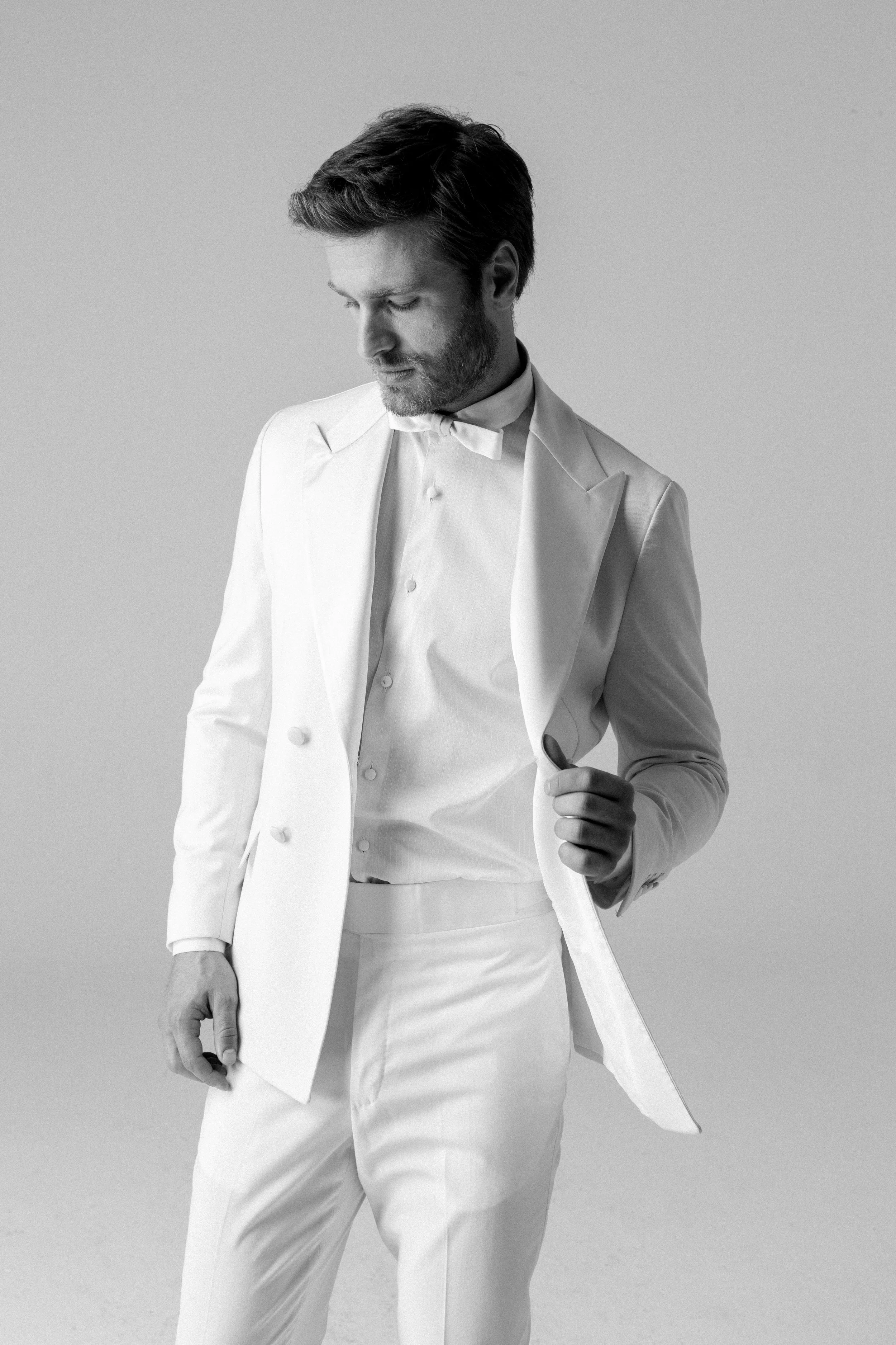 Uomo con abito bianco, posa in modo elegante, in bianco e nero.
