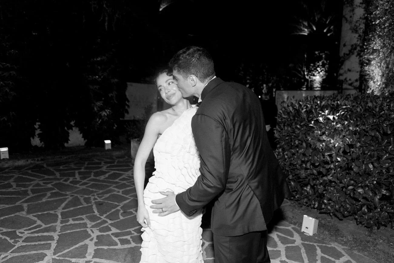 Due persone in abiti formali si baciano in un giardino al chiaro di luna.