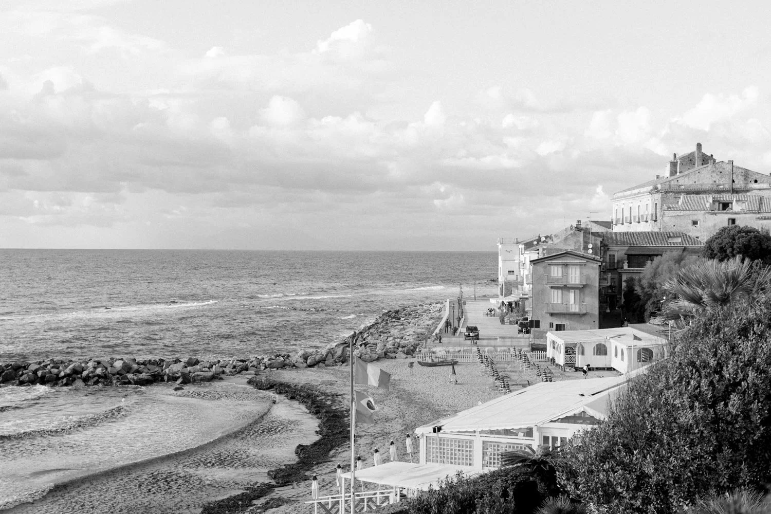 Vista di un litorale con mare, rocce e edifici lungo la costa, con nuvole nel cielo.