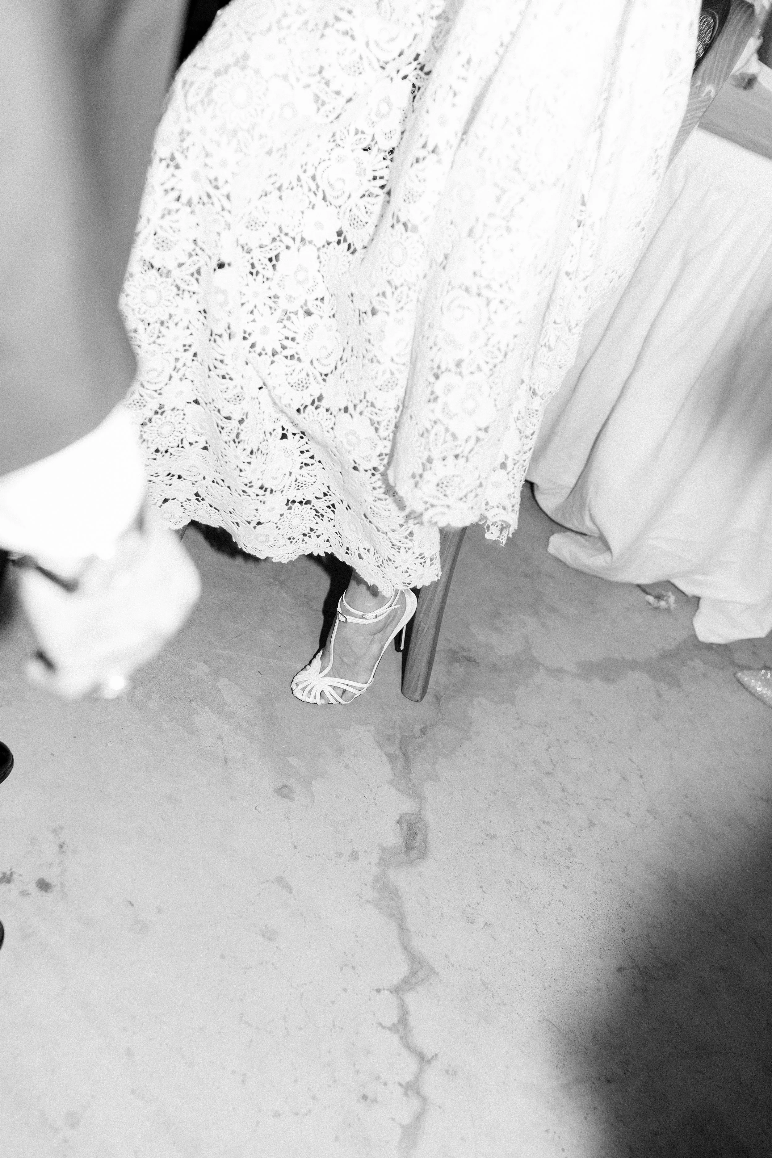 Scarpa donna in sandalo bianco con tacco alto, vista dal basso, sopra un pavimento di cemento con una crepa visibile