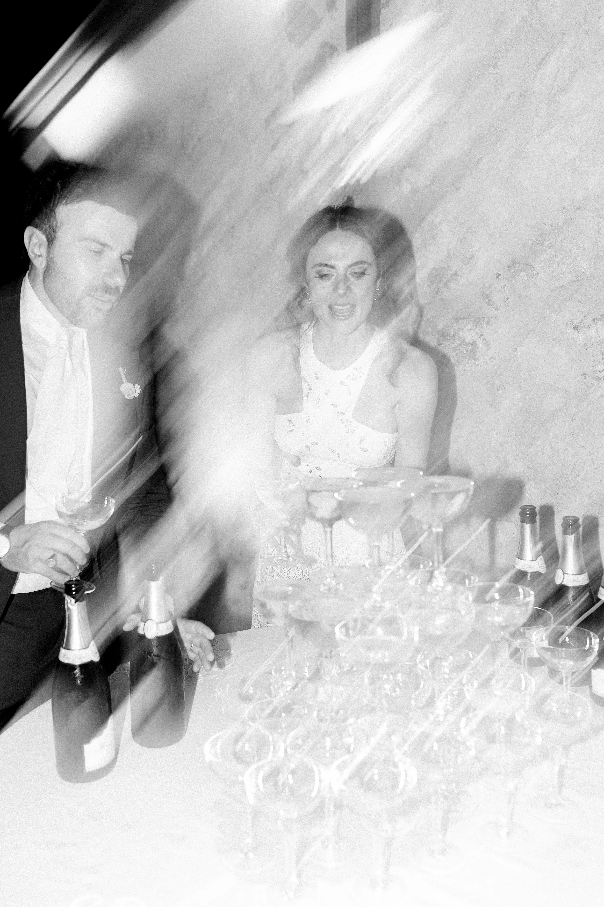 Due persone che brindano con champagne in un evento festivo, con bicchieri e bottiglie di champagne su un tavolo, in un ambiente eleganti.