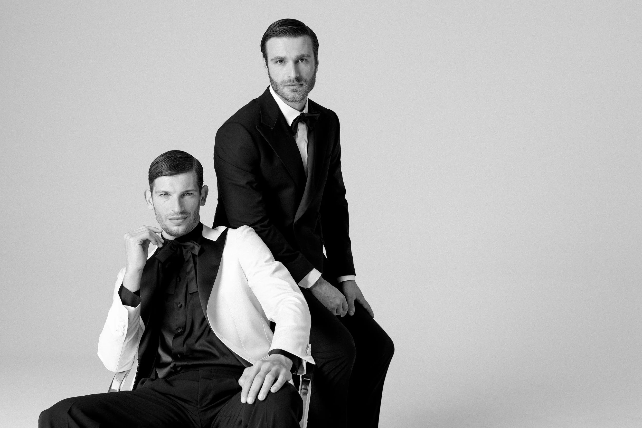 Due uomini eleganti in abiti formali neri e bianchi, uno seduto e uno in piedi, in stile black e white