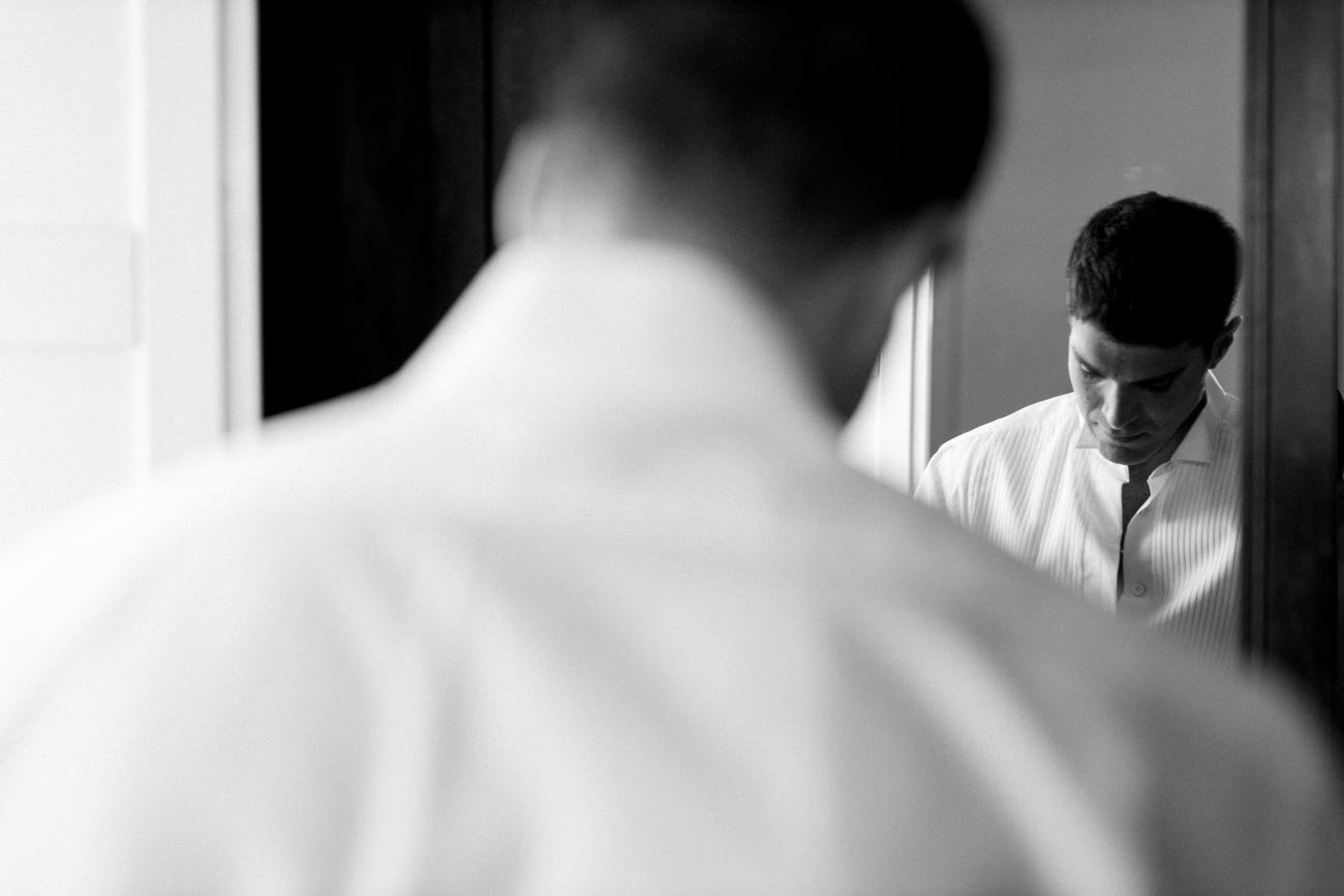 Uomo che si guarda allo specchio in una stanza con illuminazione soffusa.