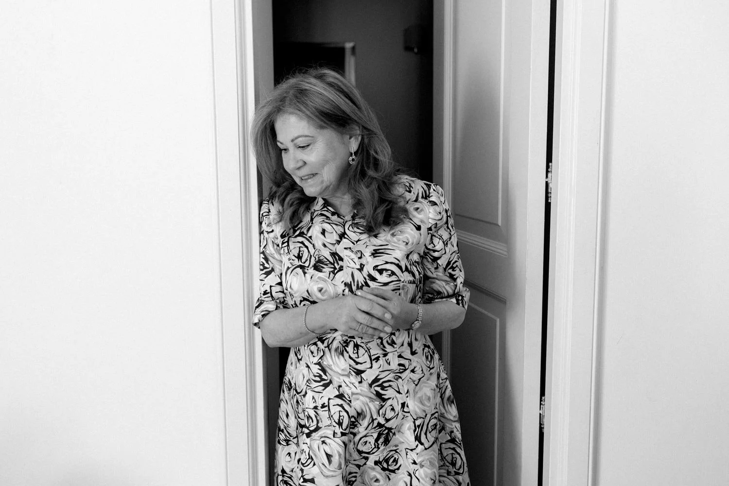 Una donna con un abito a fiori prende il tavolo mentre sorride, evidente in una stanza con pareti chiare.