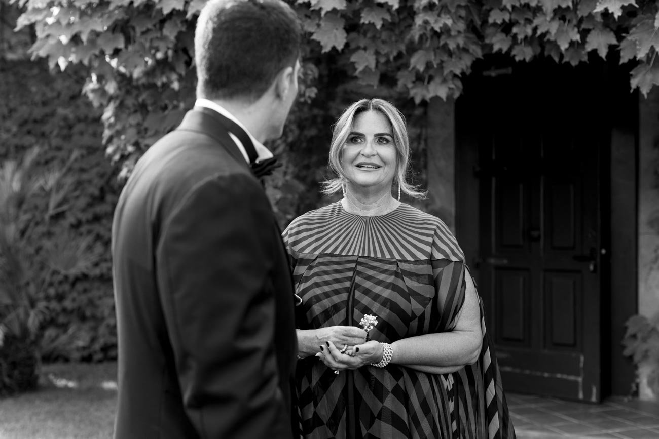 Una donna sorride mentre parla con un uomo in un giardino, entrambi vestiti elegantemente, in un contesto formale o romantico.