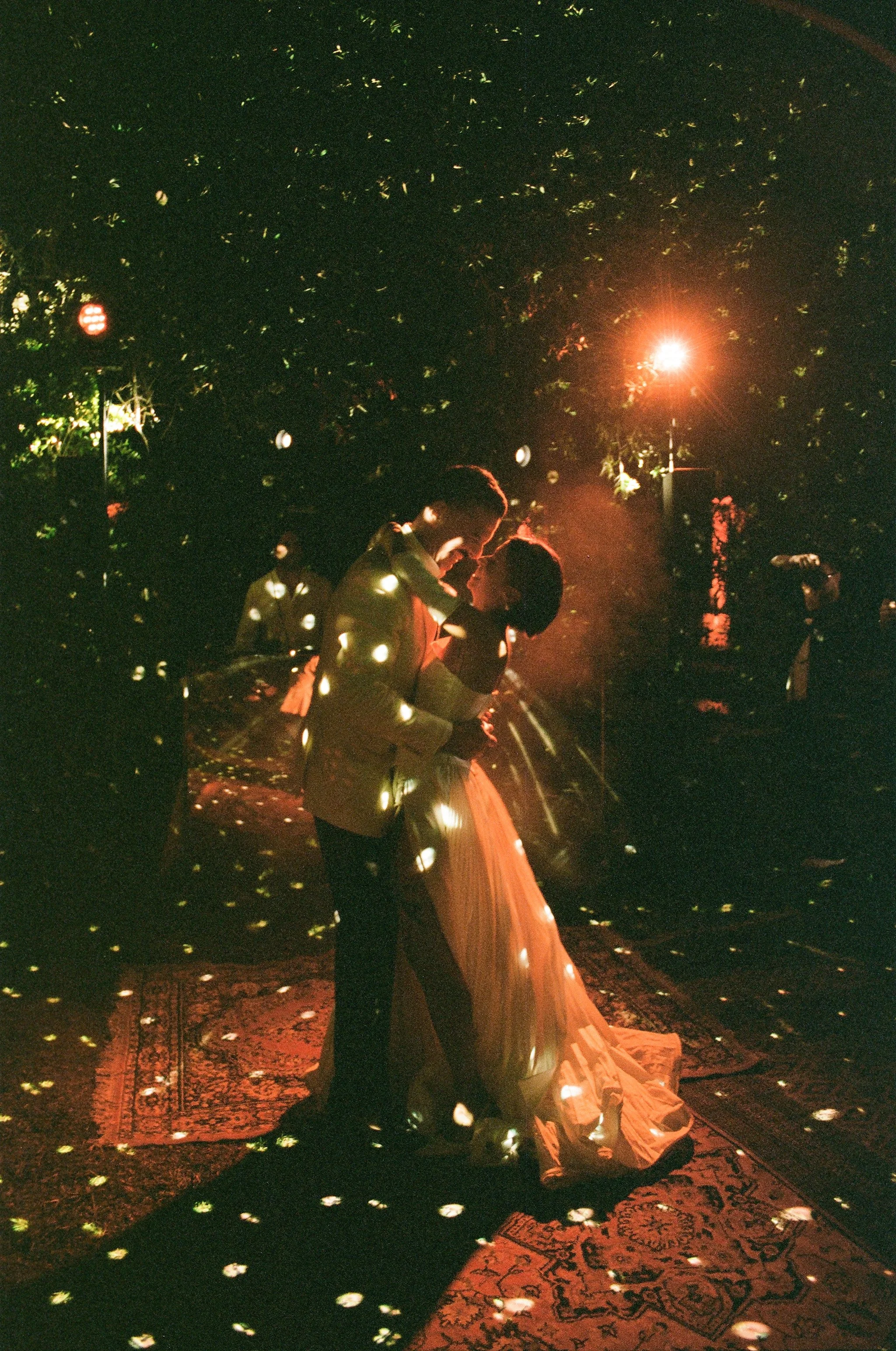 Una coppia si sposa si abbraccia sotto luci soffuse e riflessi di luci colorate in un'atmosfera romantica.