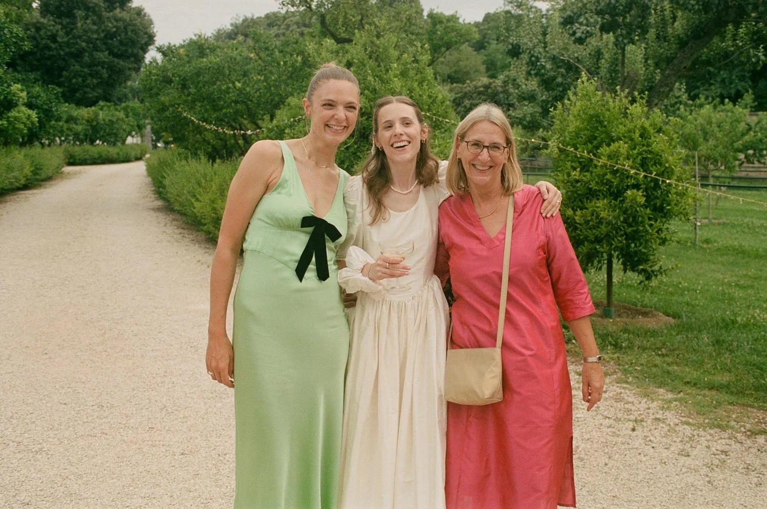 Tre donne sorridenti che camminano insieme in un prato, con alberi e cespugli sullo sfondo, durante un evento all'aperto.