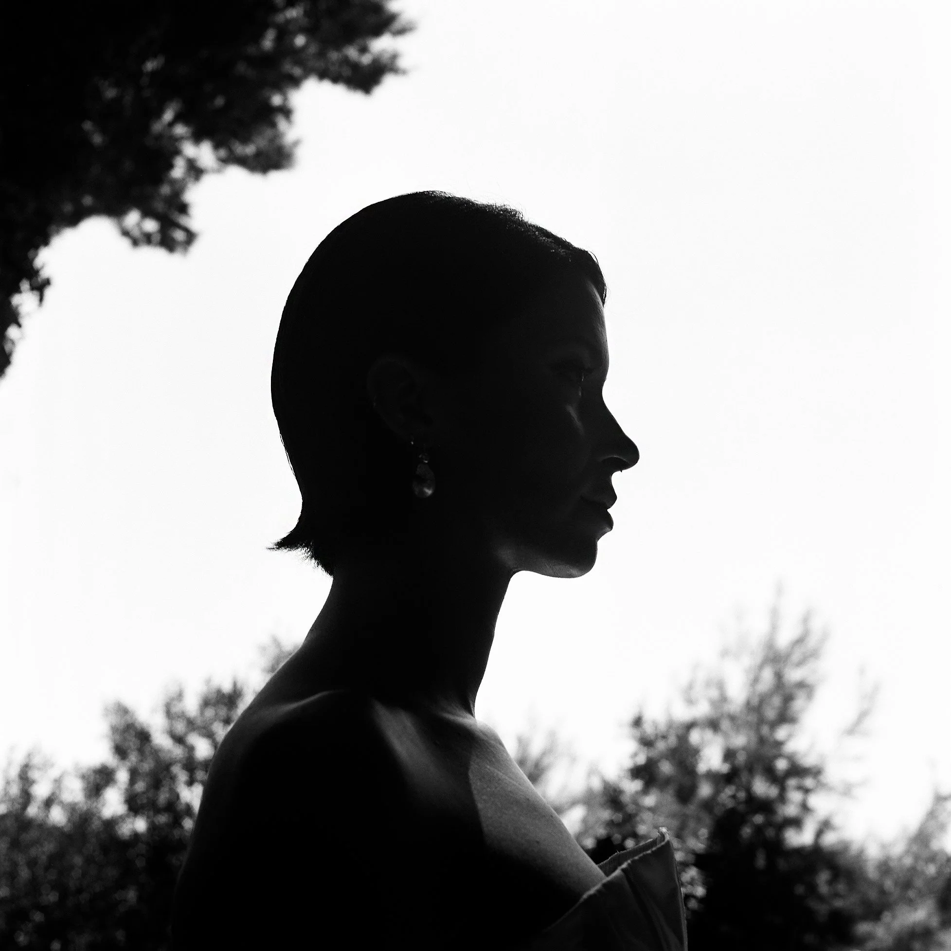 Silhouette di una donna con orecchini, vista di profilo, con sfondo di cielo e alberi