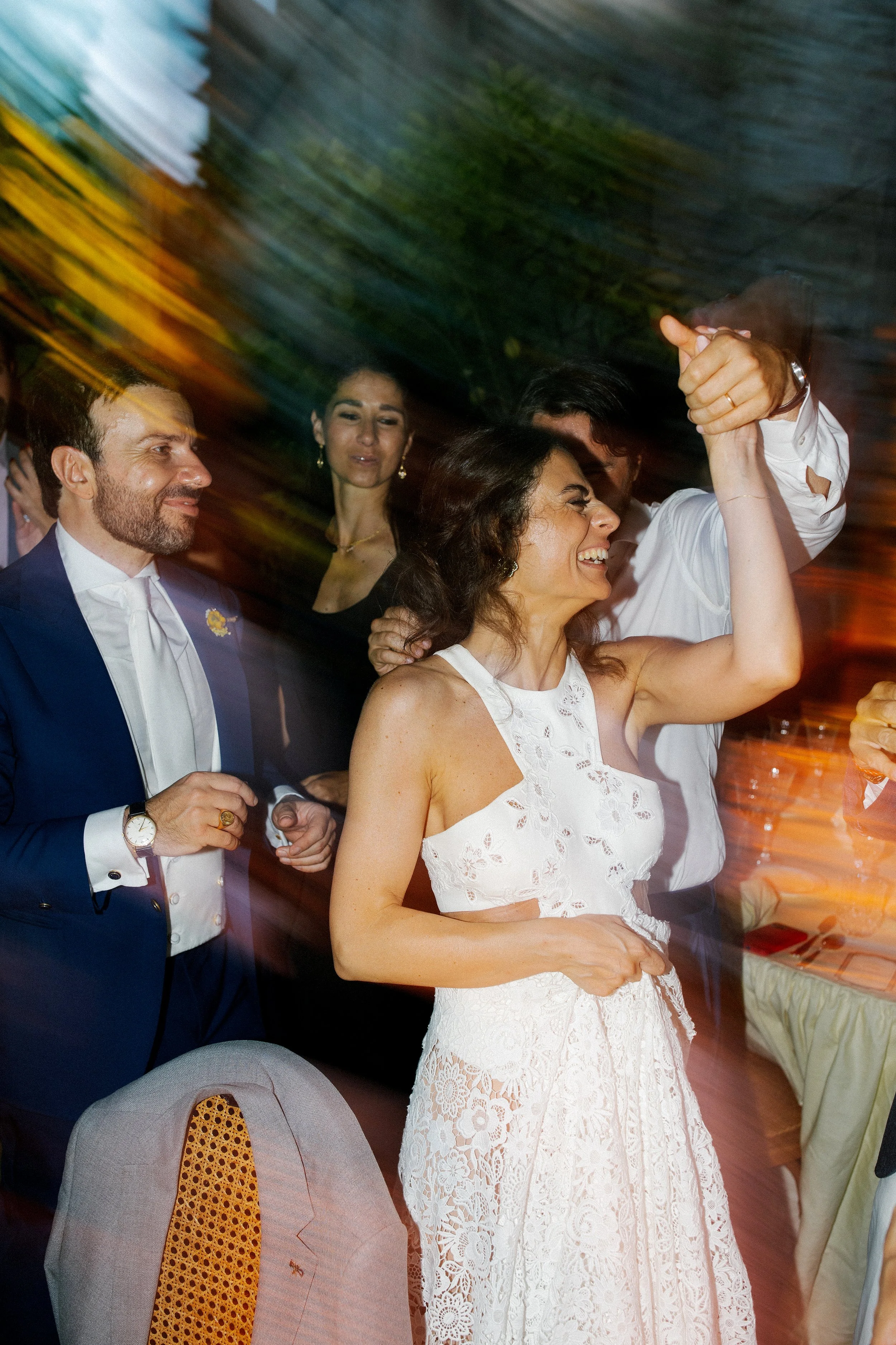 Persone che si divertono a una festa, con alcune che ballano e ridono, in un ambiente illuminato con luci colorate.