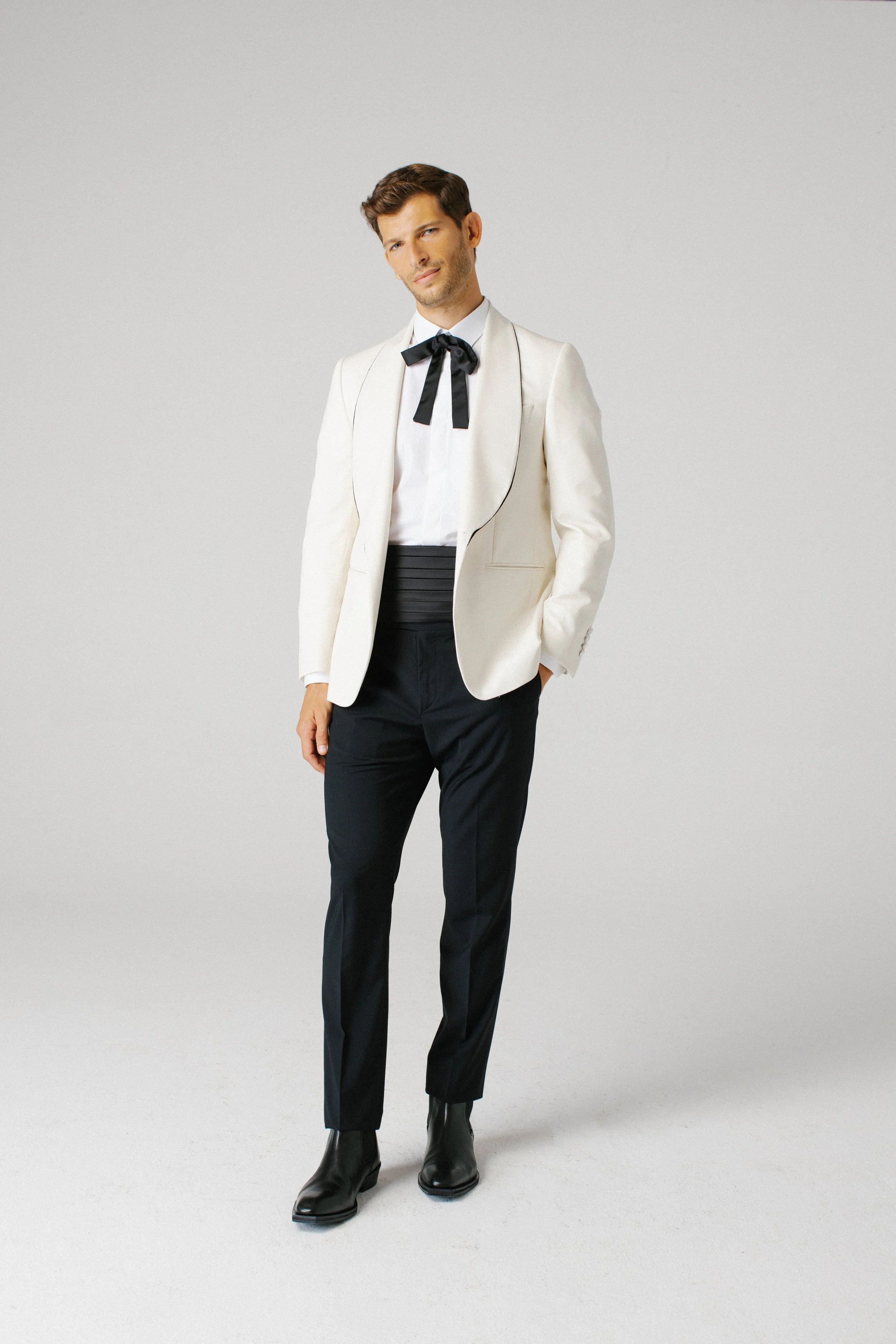 Uomo vestito con giacca bianca, pantaloni neri, camicia bianca e fiocco nero.