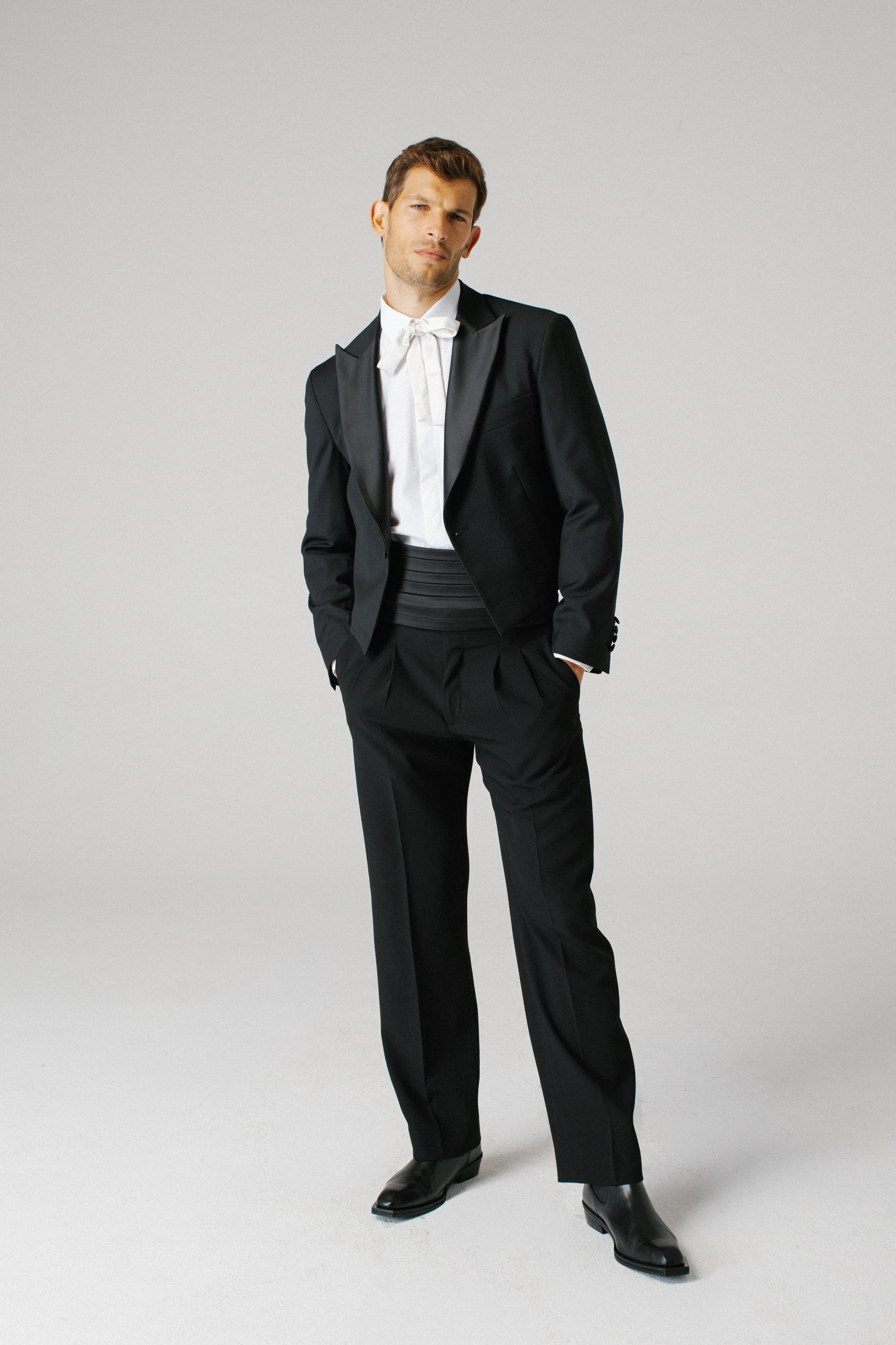 Uomo in completo nero con camicia bianca e cravatta, in posa con mani in tasca
